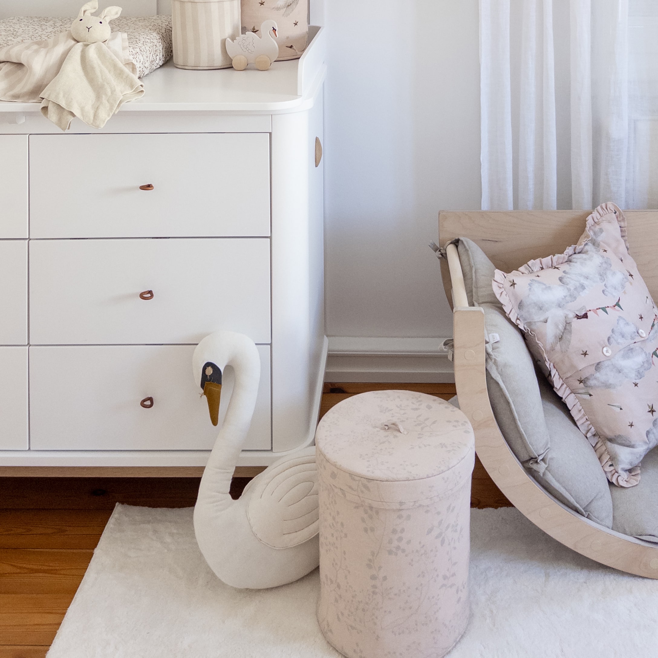 Camera per bambini accogliente con cassettiera bianca, cigno di peluche e pouf rosa cipria in tessuto