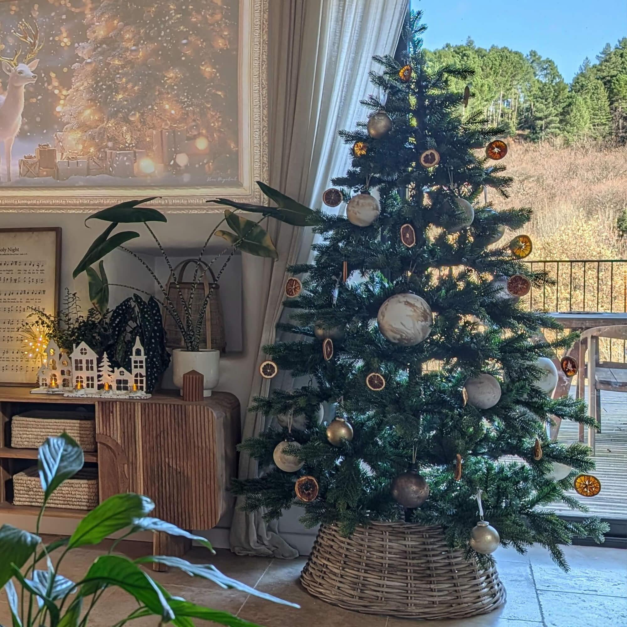 Albero di Natale con decorazioni naturali e base in vimini in ambiente accogliente con vista sul bosco
