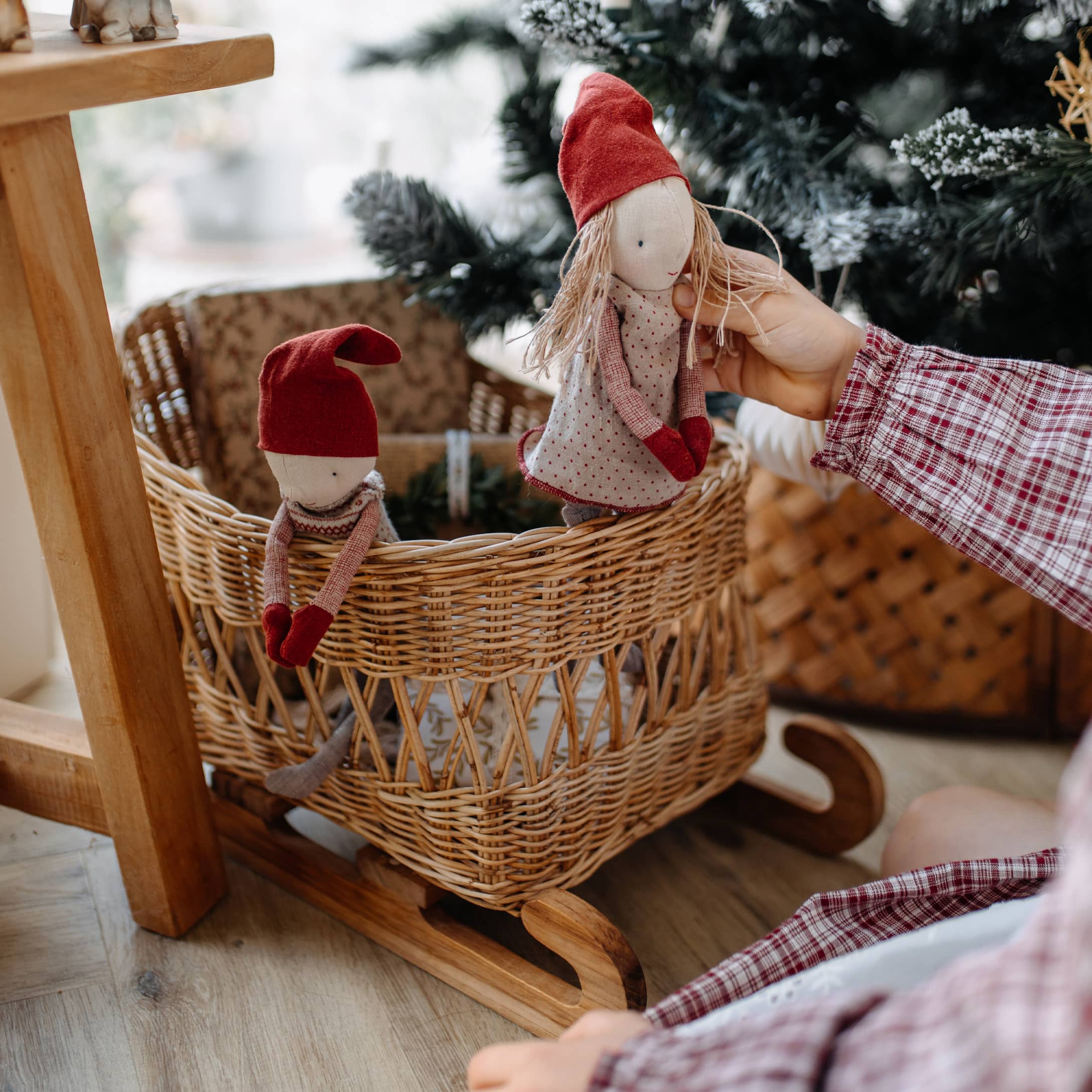 Culla a dondolo in legno con cesta in vimini e due bambole con cappelli rossi, decorazione natalizia