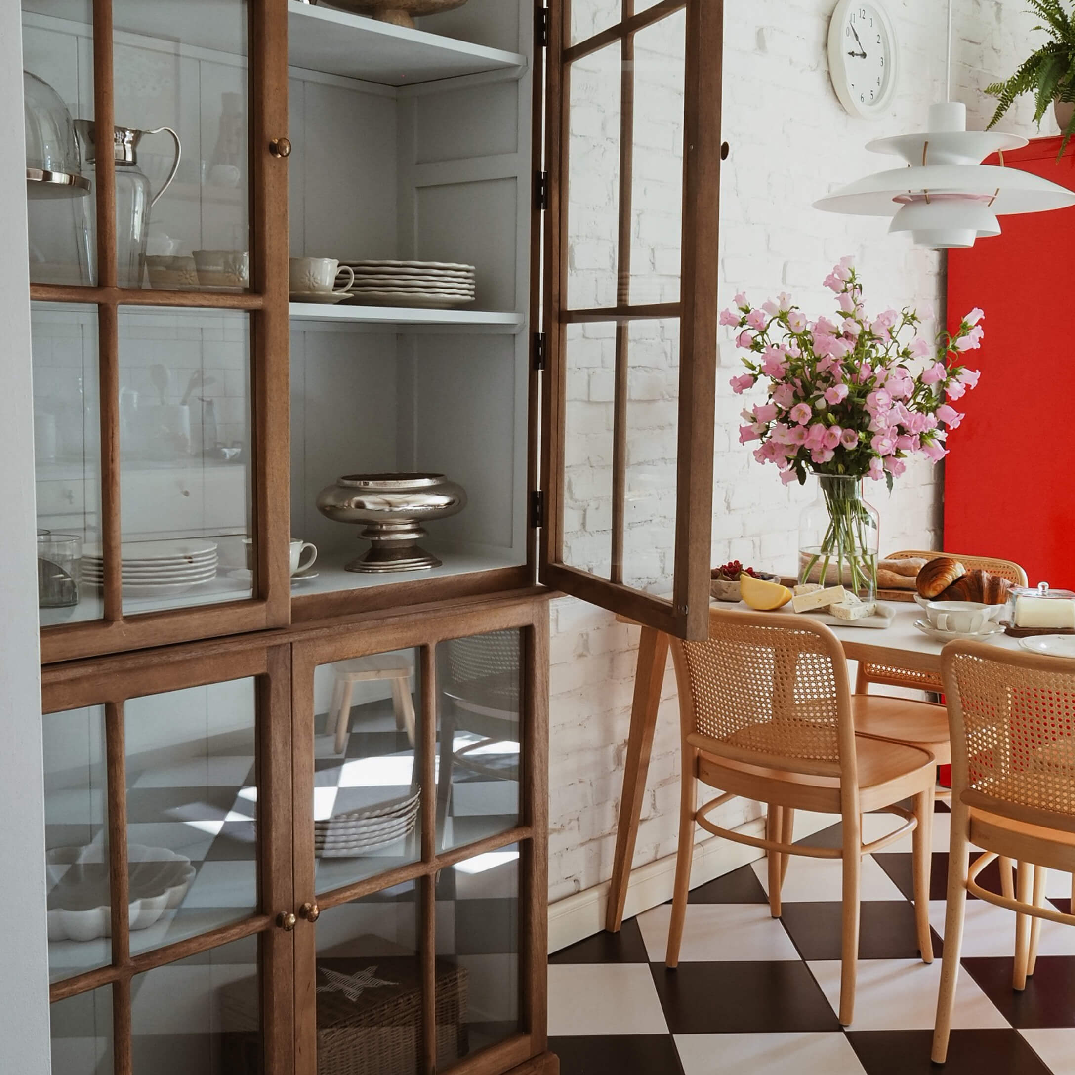 Sala da pranzo luminosa con vetrina in legno, fiori rosa e pavimento a scacchi bianco e nero