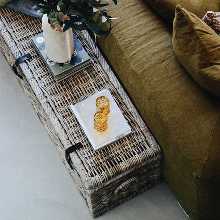 Tavolino in rattan colore naturale con decorazioni e divano verde oliva accanto, stile scandinavo