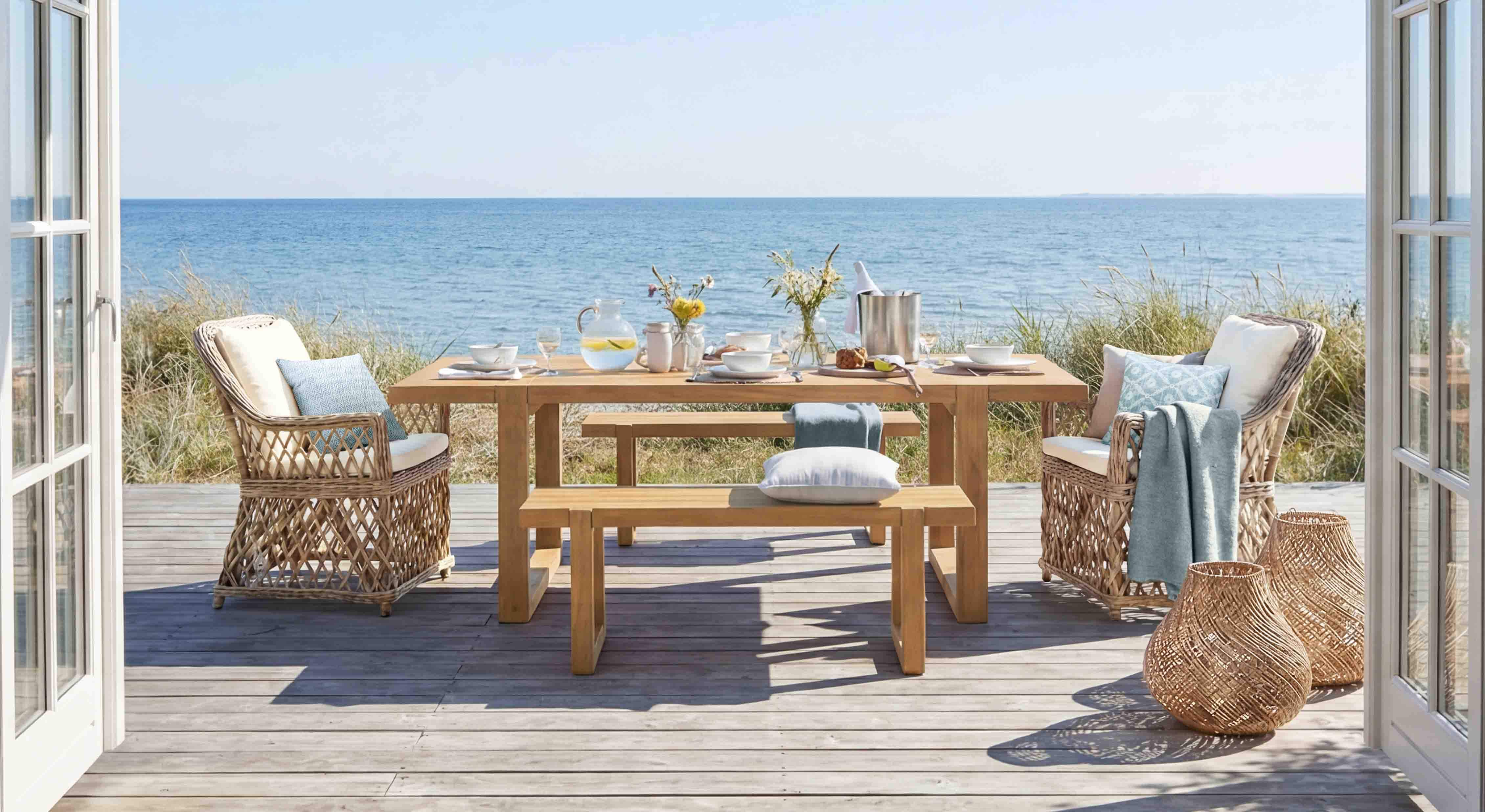 Set di mobili da giardino in legno e rattan in colori naturali su terrazza con vista mare