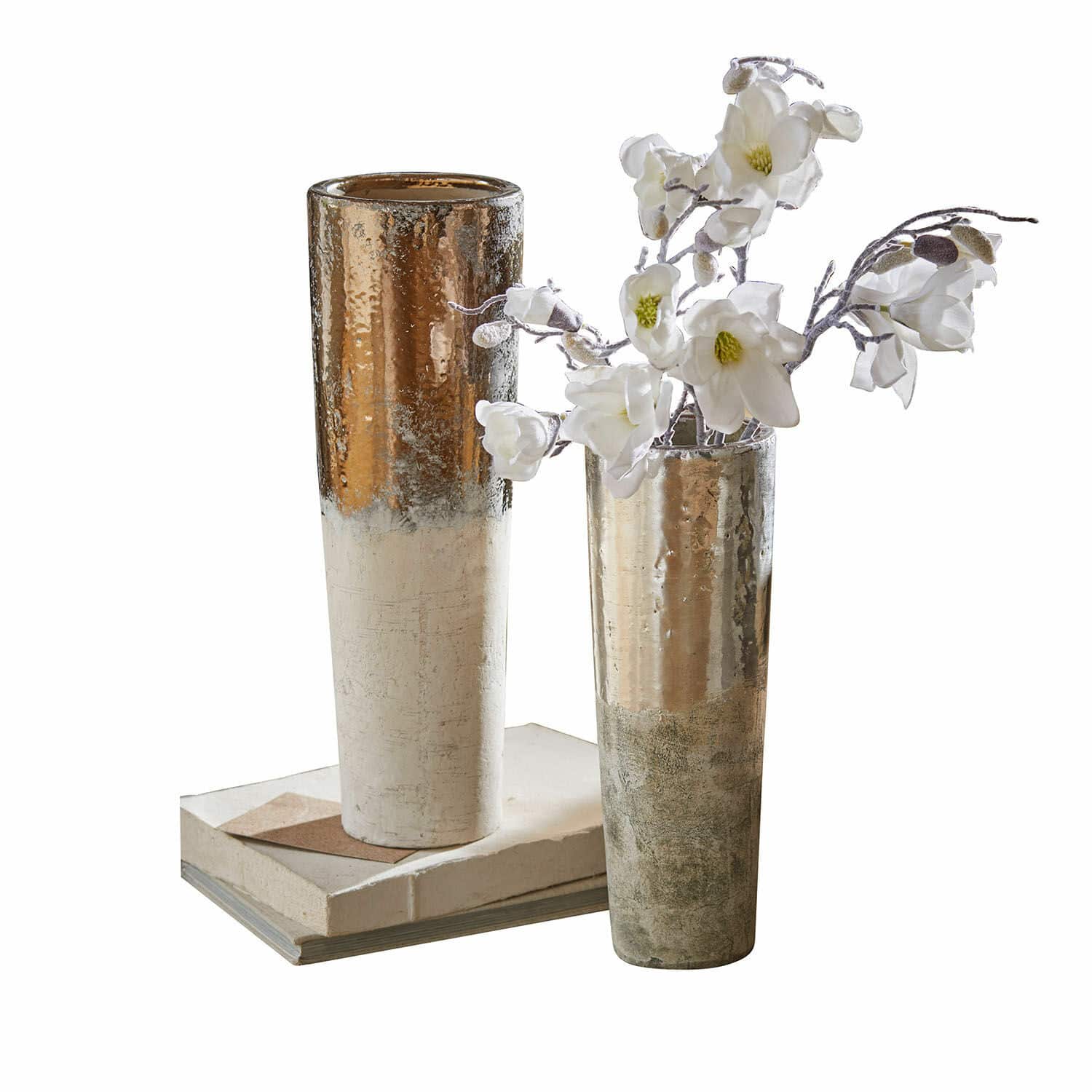 Coppia di vasi Tameena Due vasi metallici alti color oro e argento su libri con fiori bianchi decorativi