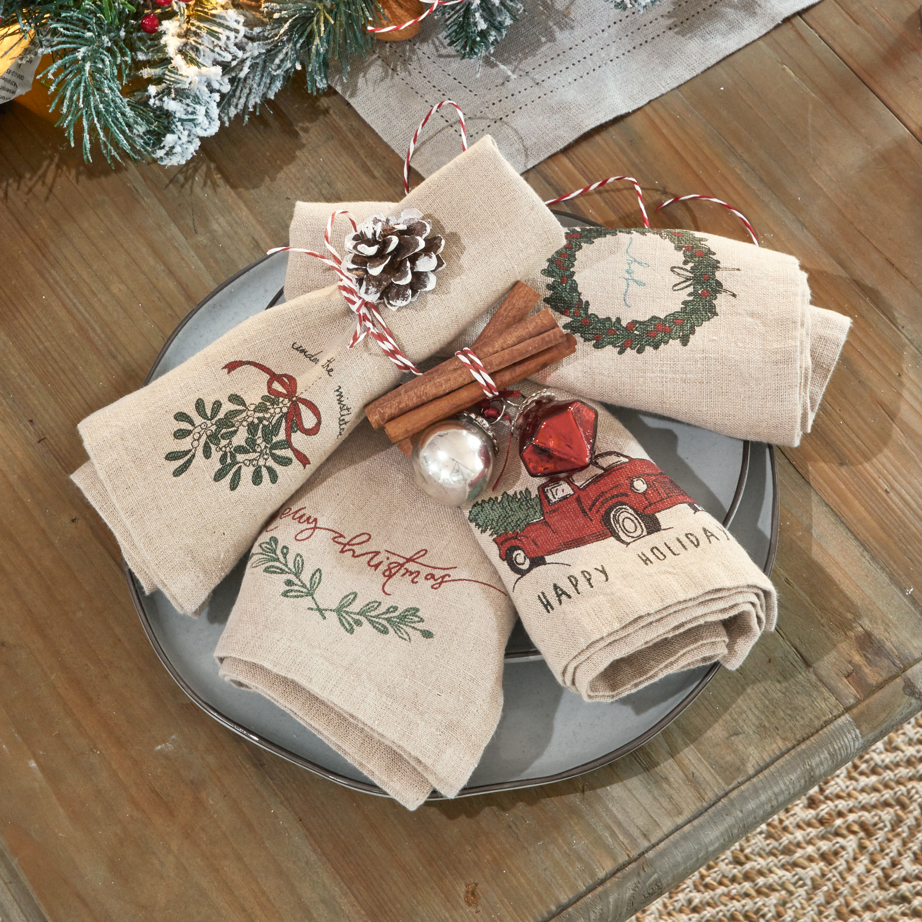Tovaglioli in lino con motivi natalizi, decorati con stecche di cannella e pigna su piatto grigio
