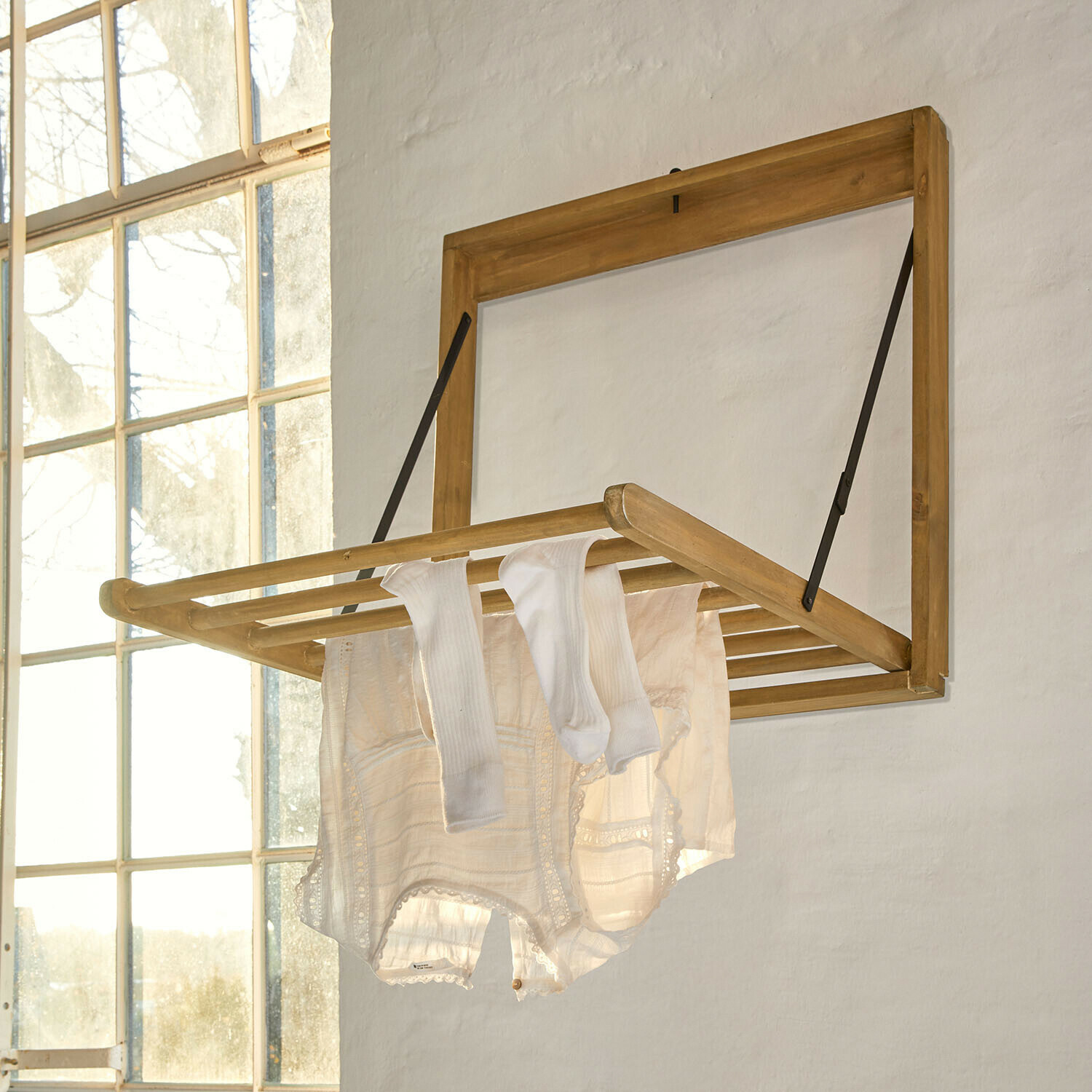 Stendibiancheria da parete Élirème Stendibiancheria a parete pieghevole in legno chiaro con vestiti bianchi in stanza luminosa