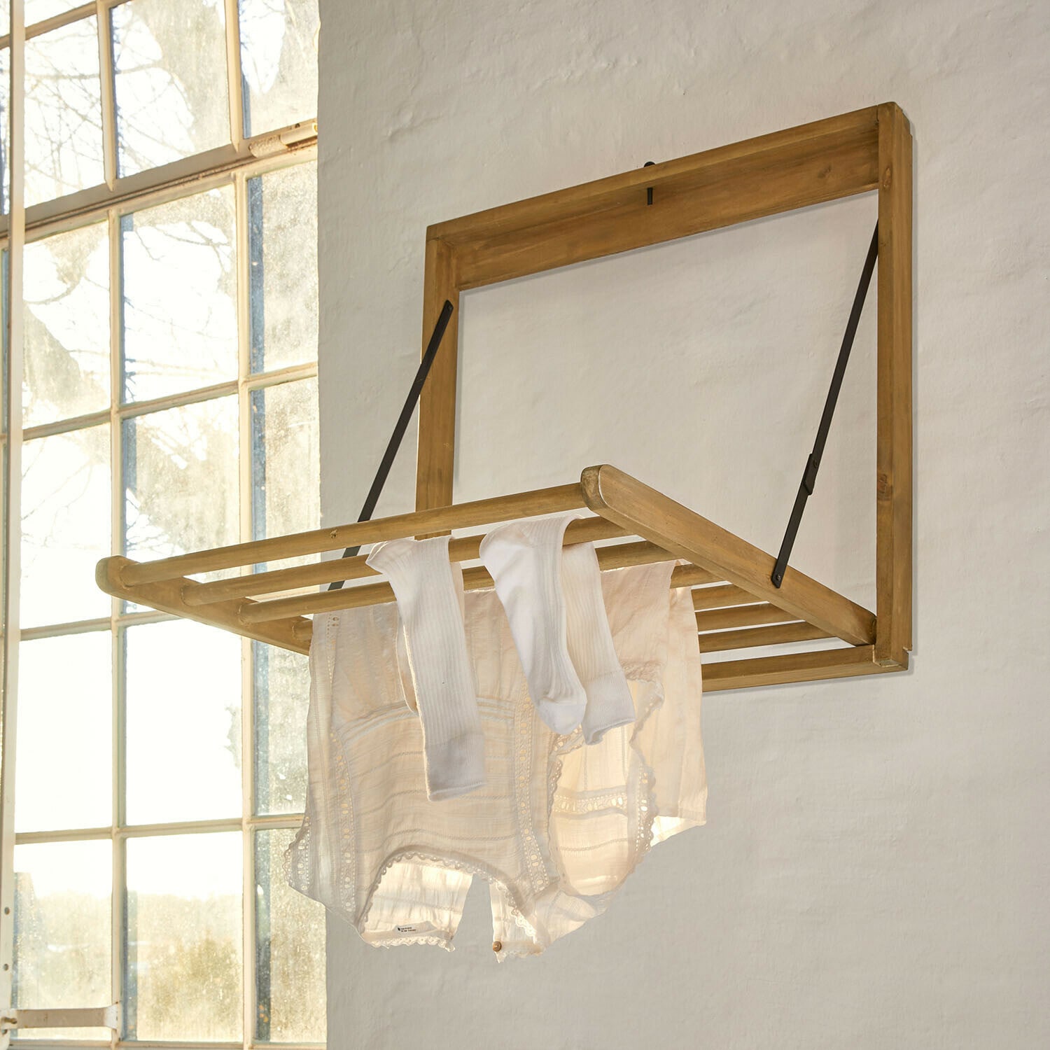 Stendibiancheria da parete Élirème Stendibiancheria a parete pieghevole in legno chiaro con vestiti bianchi in stanza luminosa