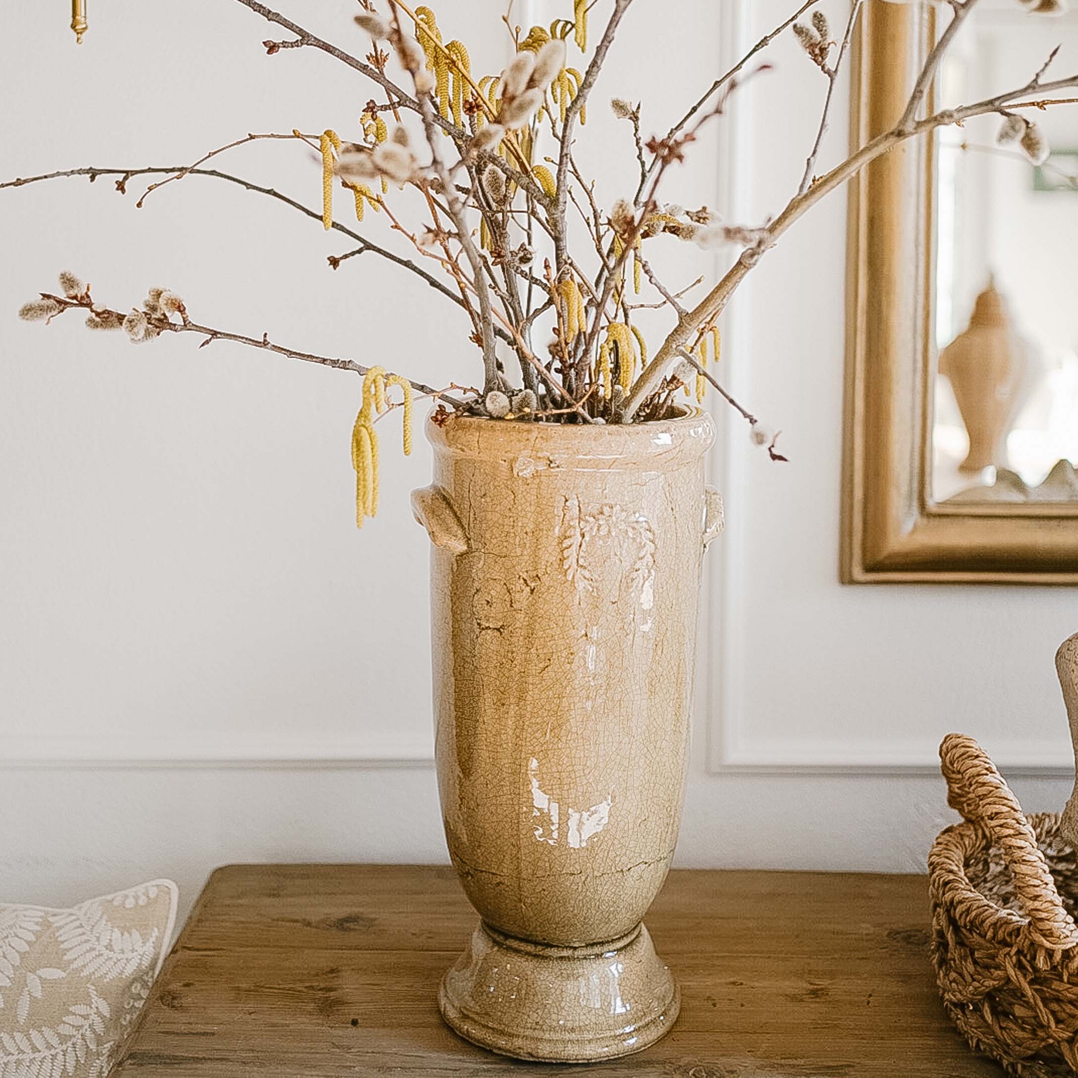 Vaso in ceramica beige con fiori e rami su tavolo in legno in interno luminoso