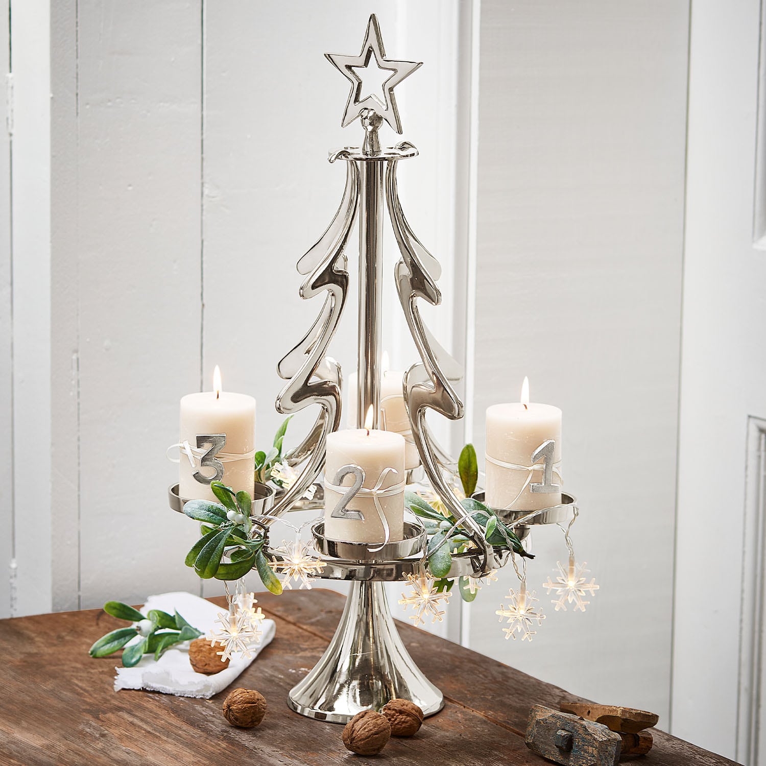 Portacandele in metallo a forma di albero con quattro candele bianche e decorazioni natalizie su tavolo in legno