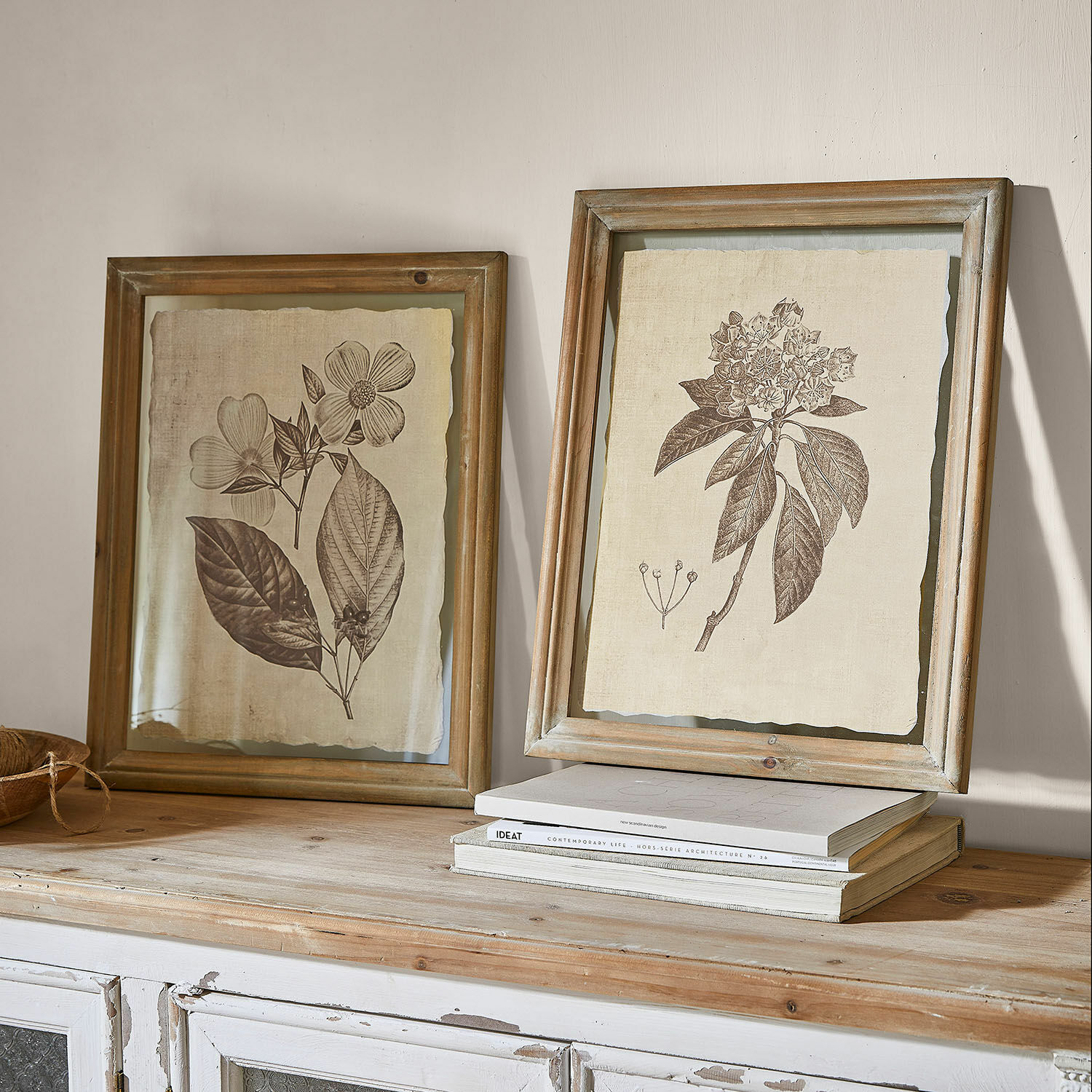 Coppia di quadri Guyra Due cornici rustiche in legno con disegni botanici di fiori su sfondo beige su un tavolo in legno
