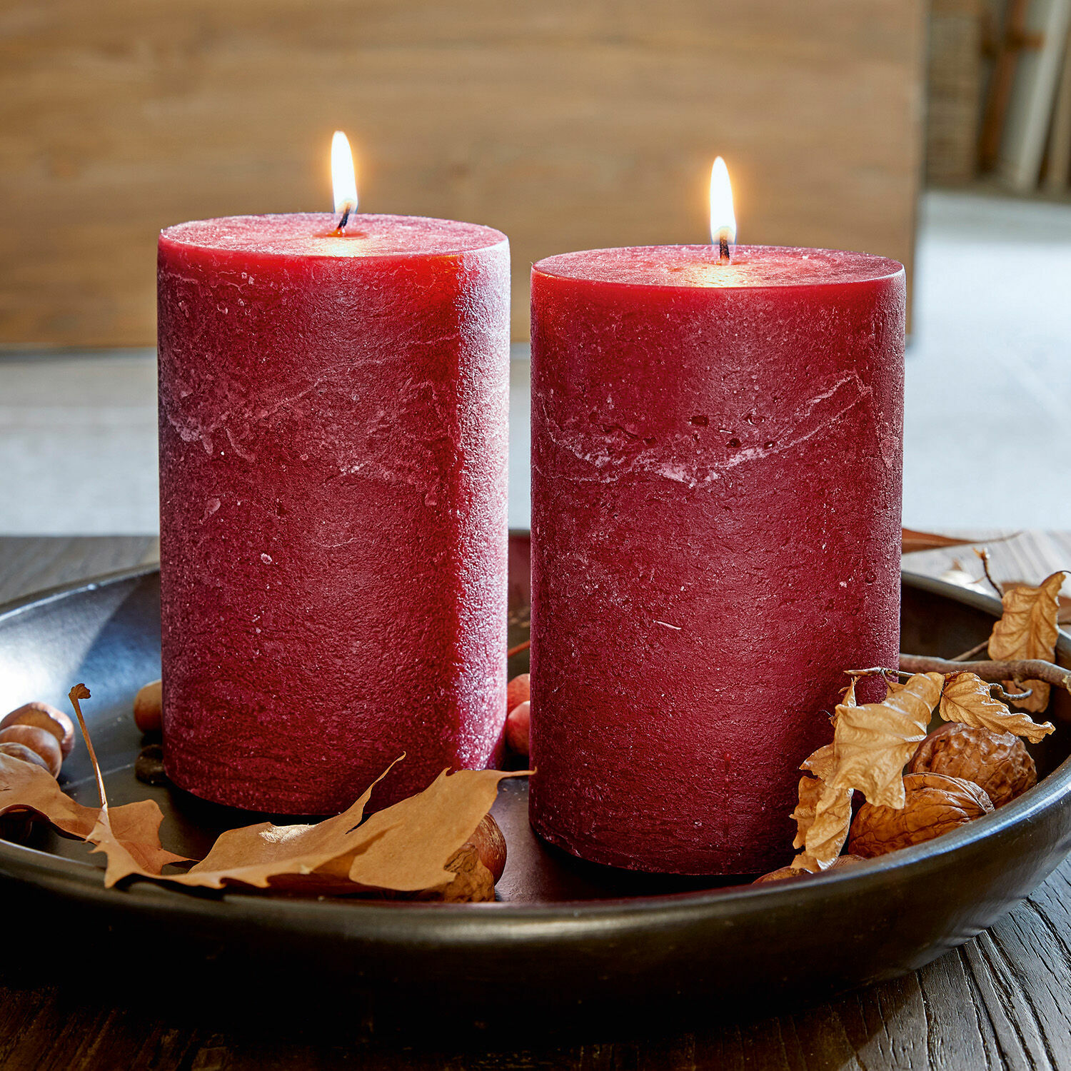Coppia di candele Oviedo Due candele rosse in cera su un vassoio nero con foglie secche e noci, decorazione autunnale