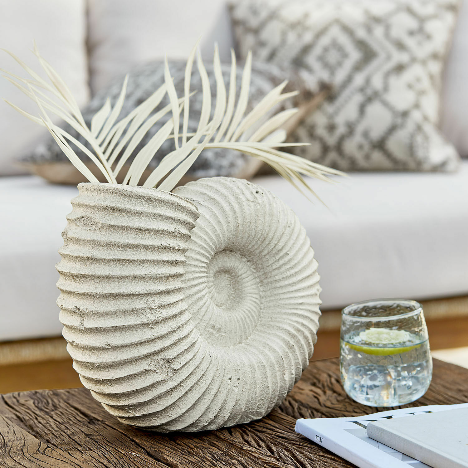 Vaso Korrellin Vaso decorativo in cemento a forma di conchiglia con foglie chiare su tavolo in legno in soggiorno