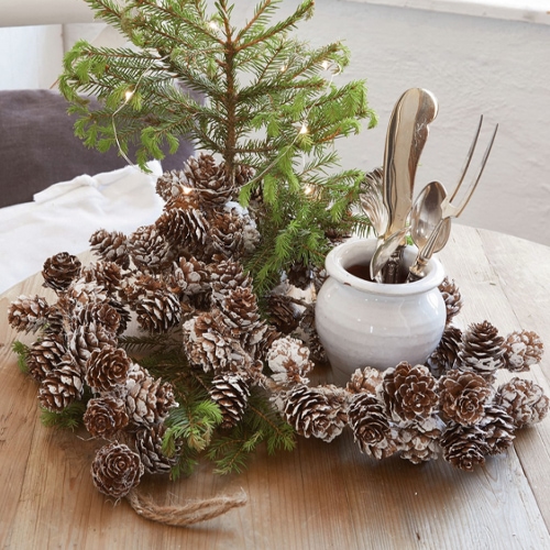 Corona decorativa di pigne con effetto neve su tavolo in legno, decorazione natalizia naturale