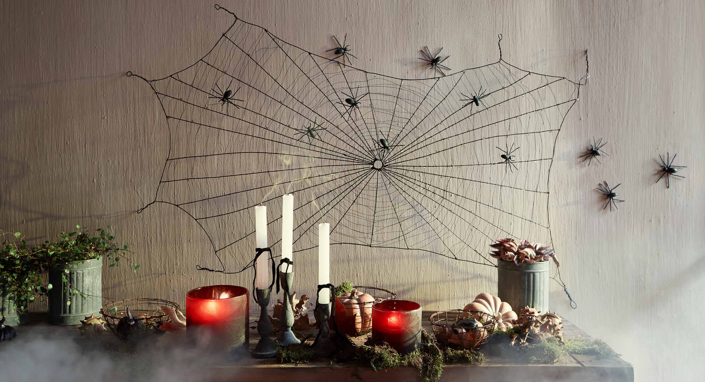 Decorazione di Halloween con ragnatela nera e ragni sul muro, candele e zucche sul tavolo