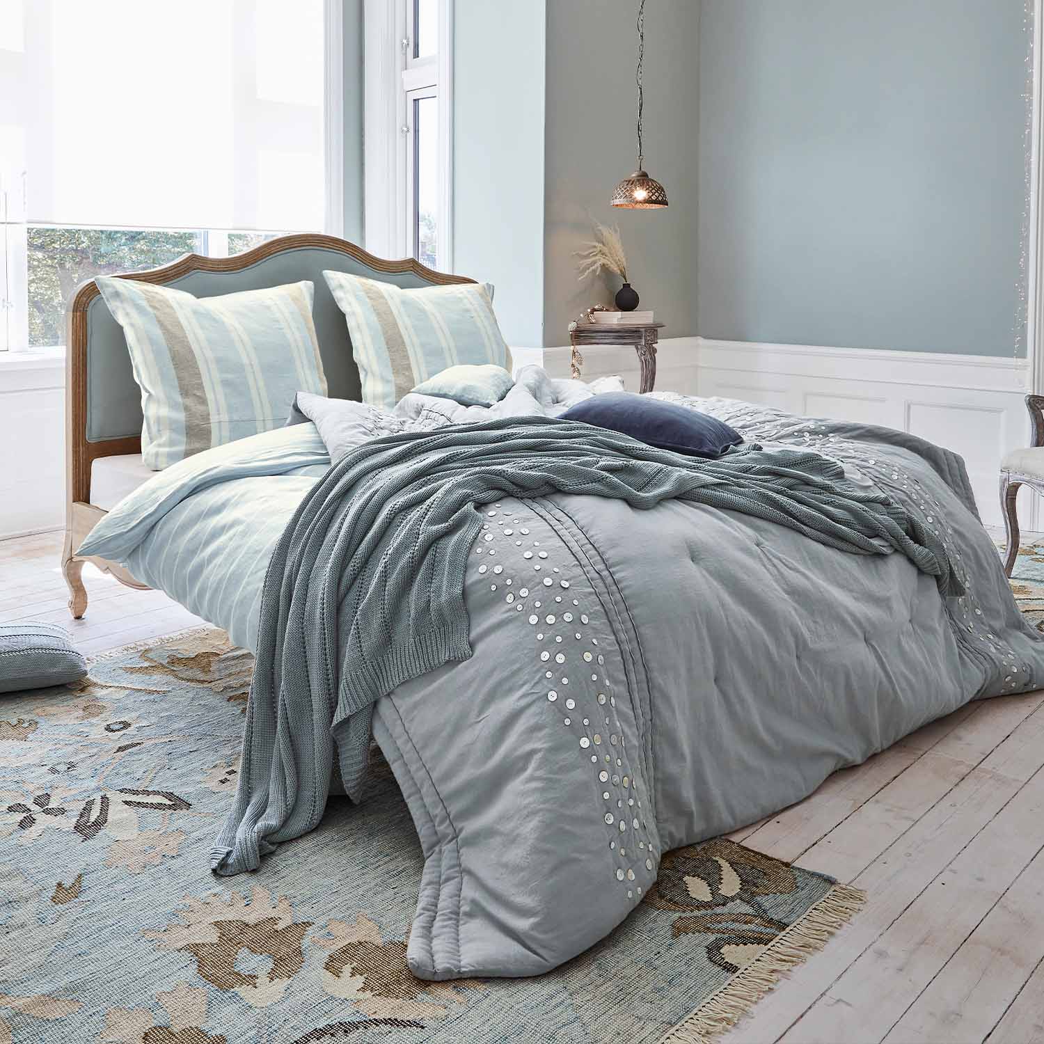 Letto con testiera in legno imbottita, biancheria da letto azzurra e coperta lavorata a maglia morbida