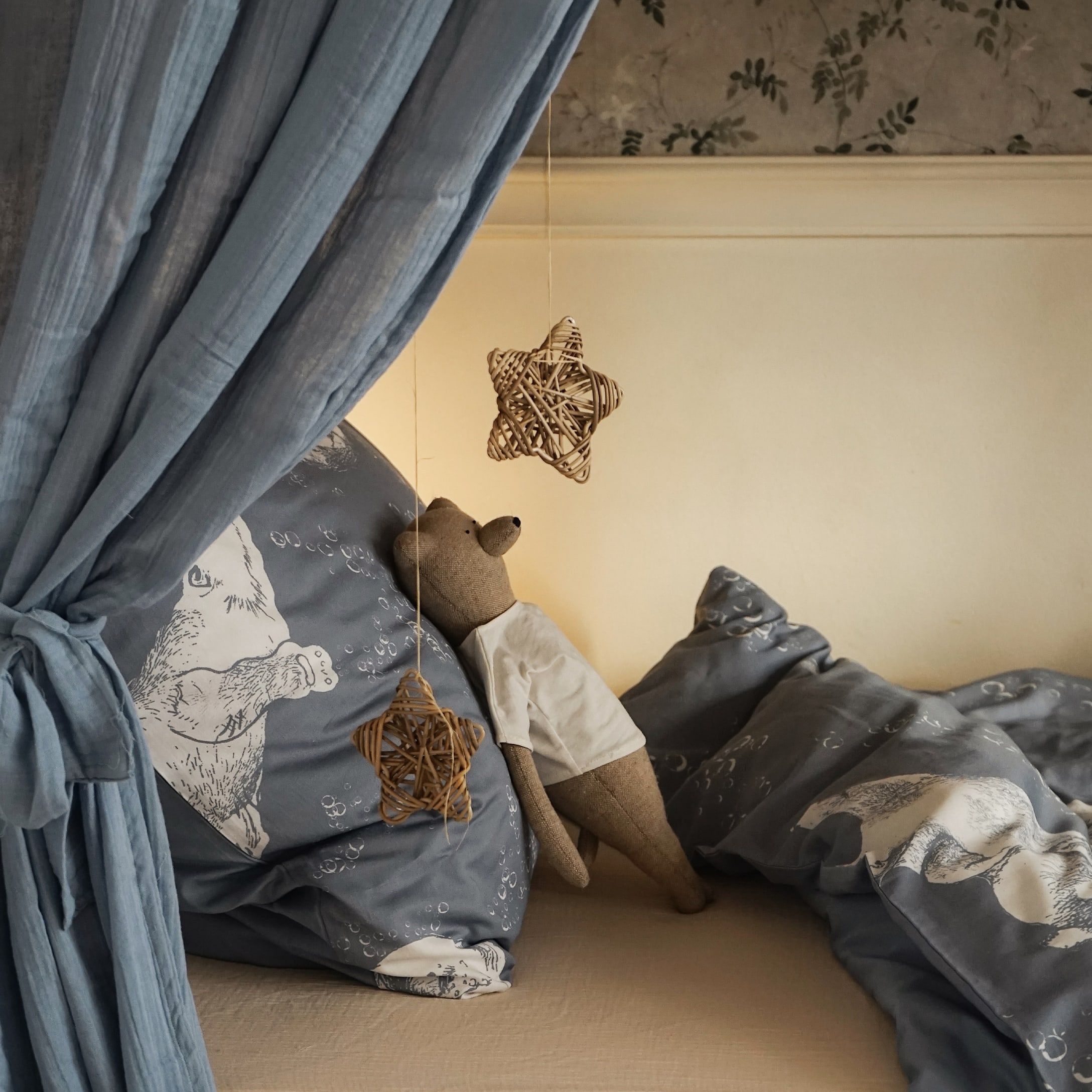 Letto accogliente con biancheria da letto blu a tema orso e orsacchiotto di stoffa, stelle di vimini appese