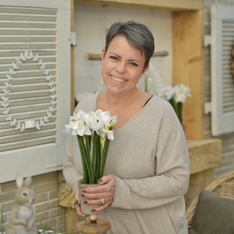 Donna che tiene vaso con fiori bianchi in ambiente naturale pasquale con decorazioni