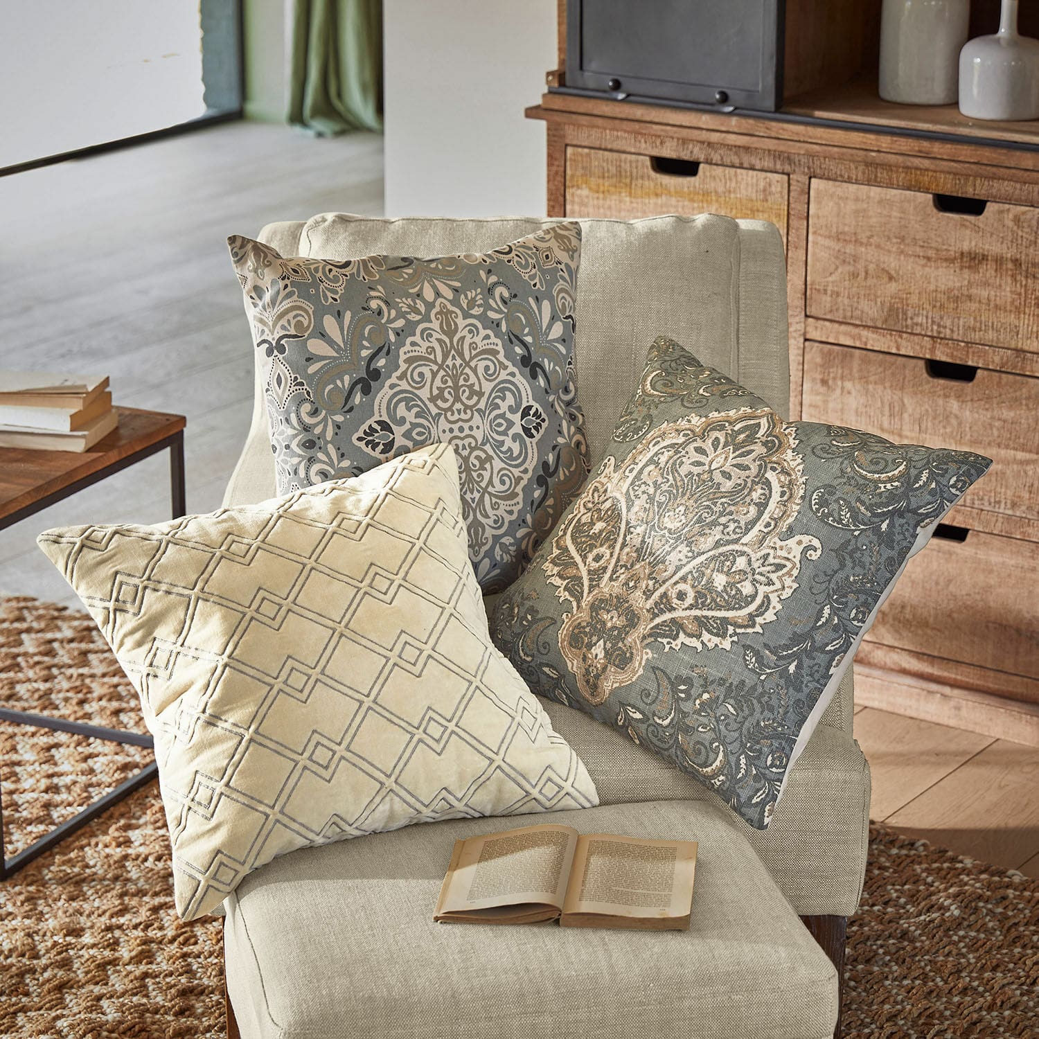 Set di 3 copricuscini Madalena Tre cuscini decorativi beige e grigi con motivi su una poltrona chiara in soggiorno