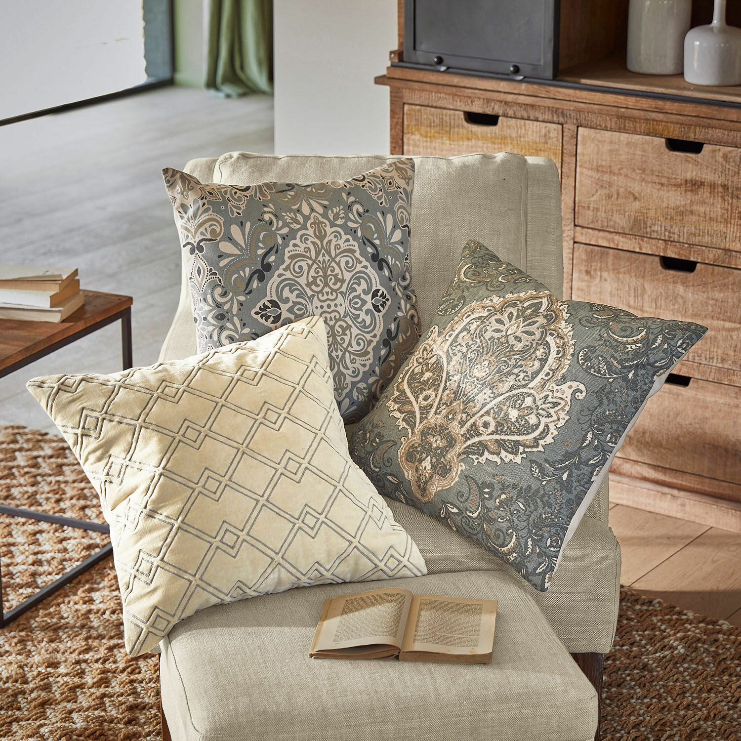 Set di 3 copricuscini Madalena Tre cuscini decorativi beige e grigi con motivi su una poltrona chiara in soggiorno