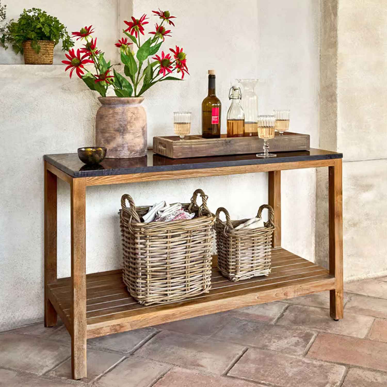 Tavolo in legno con piano nero, vaso con fiori rossi e cesti di vimini sotto in ambiente rustico