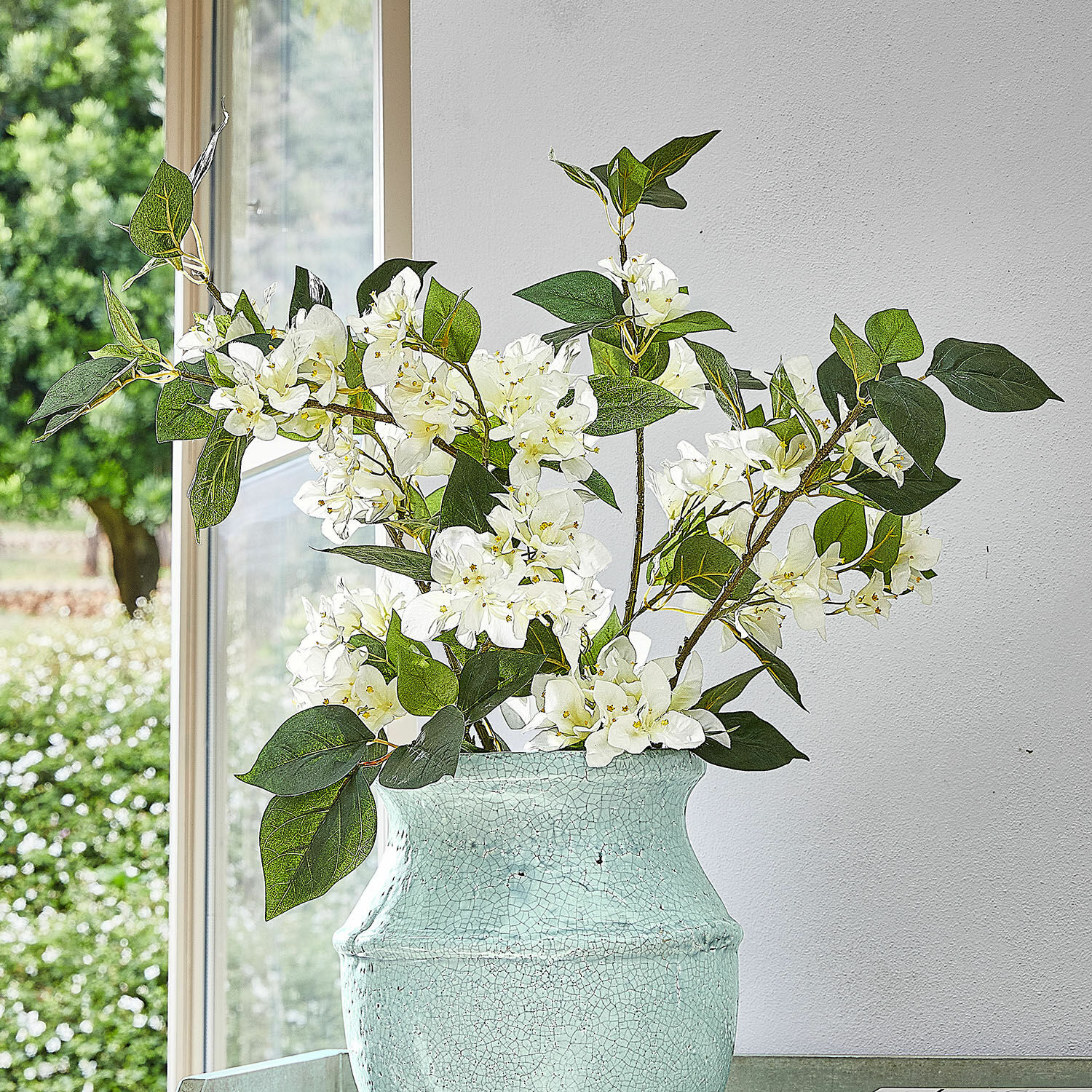 Set di 6 fiori decorativi Nireval Fiori bianchi in vaso di ceramica verde con effetto craquelé davanti a finestra e muro bianco
