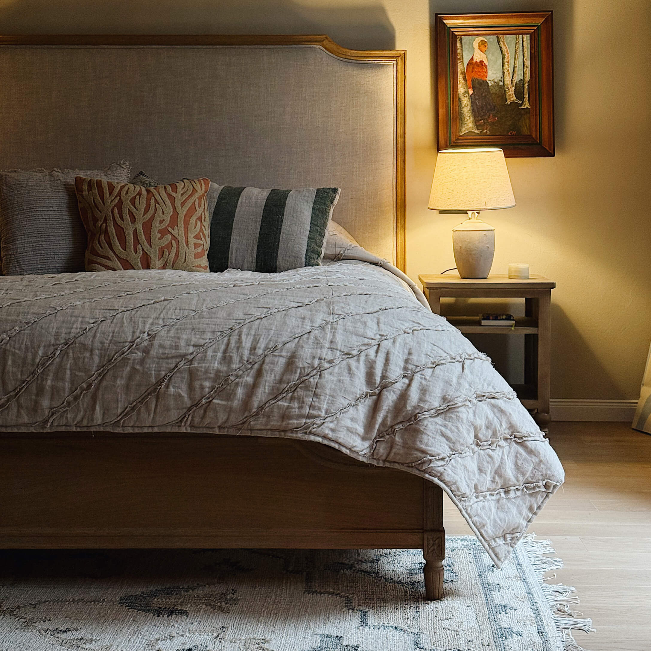 Letto in legno con testiera imbottita beige, cuscini decorativi e lampada da comodino in camera accogliente