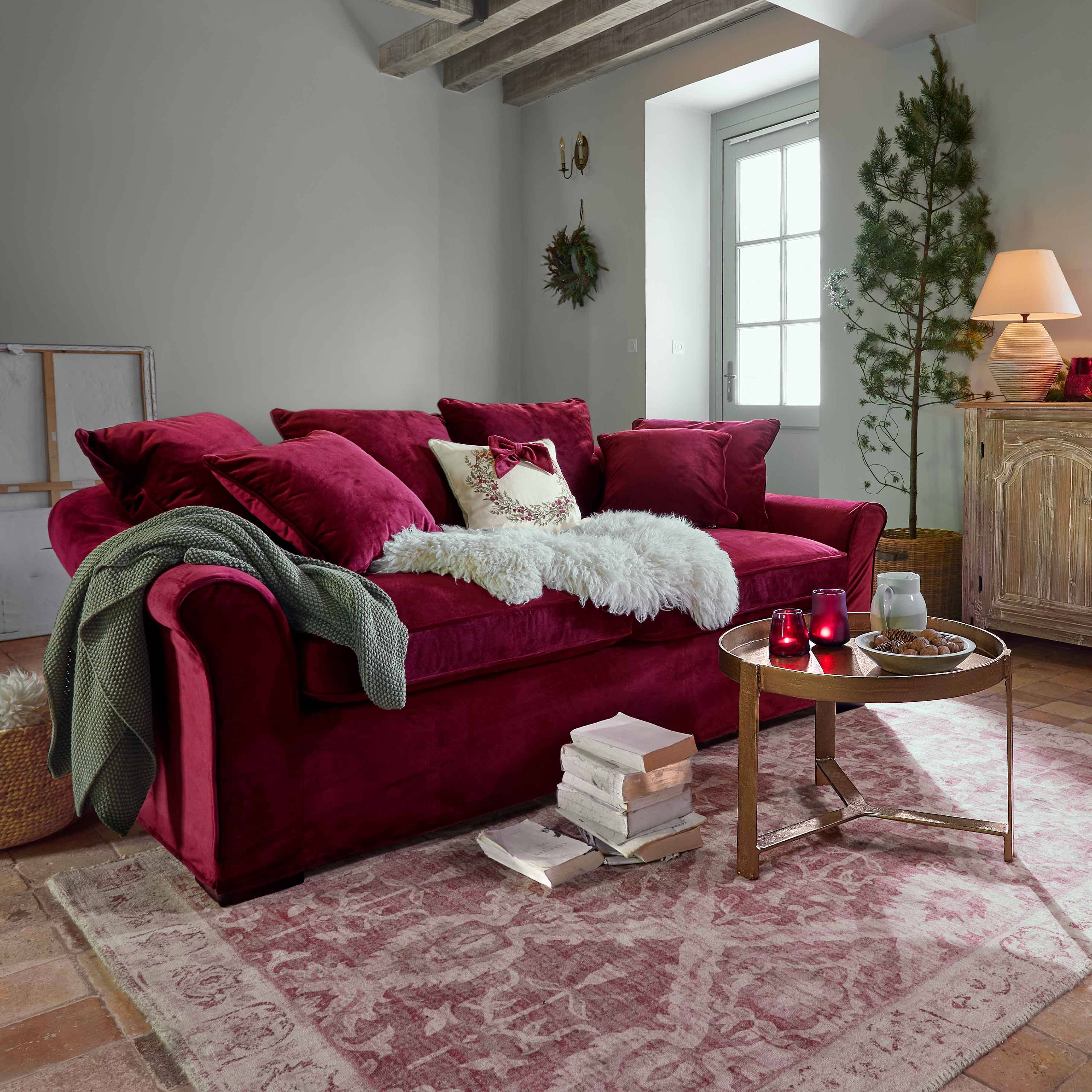 Divano in velluto bordeaux con cuscini e coperta morbida in soggiorno accogliente con travi in legno
