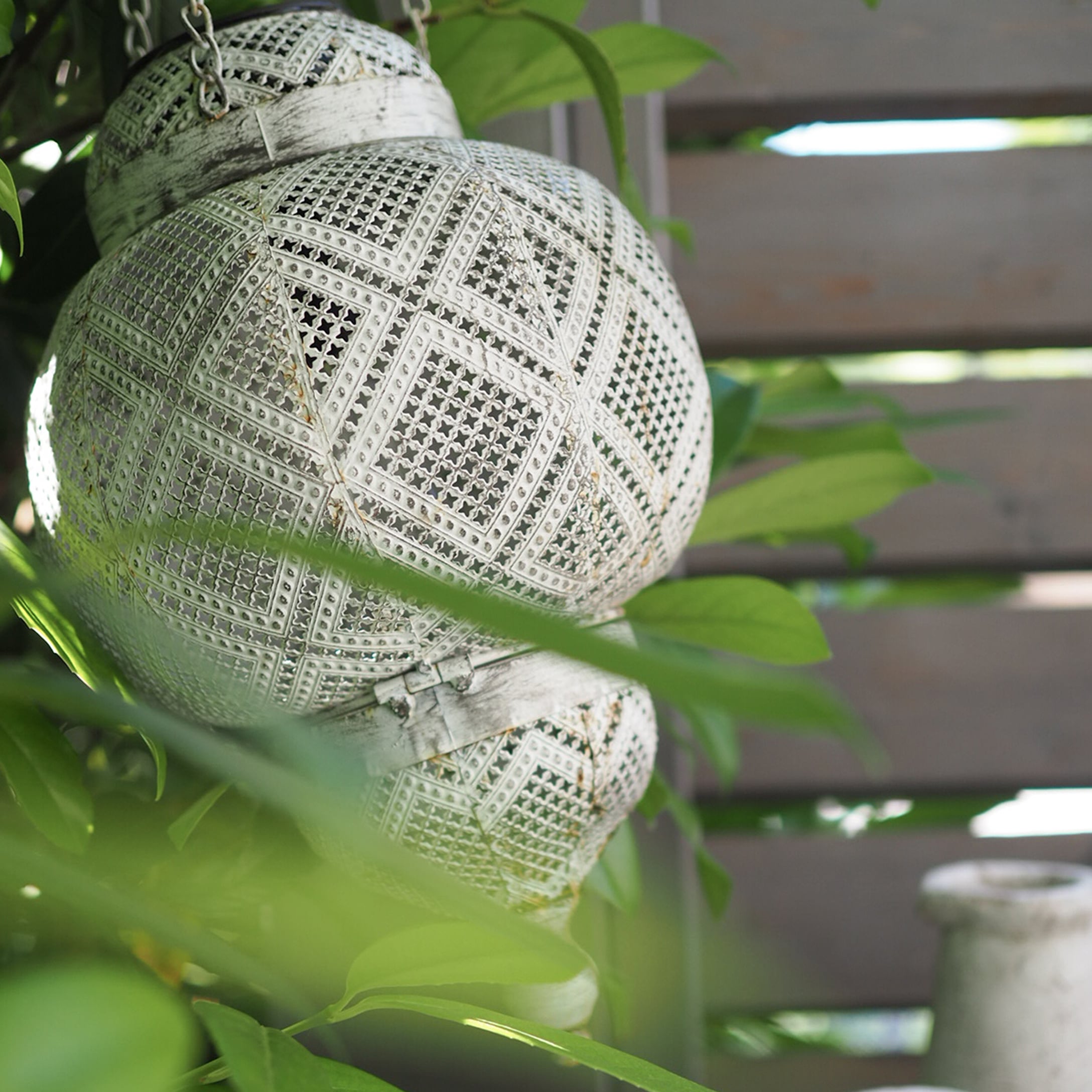 Lanterna sospesa in metallo traforato bianco tra foglie verdi per decorazione da giardino