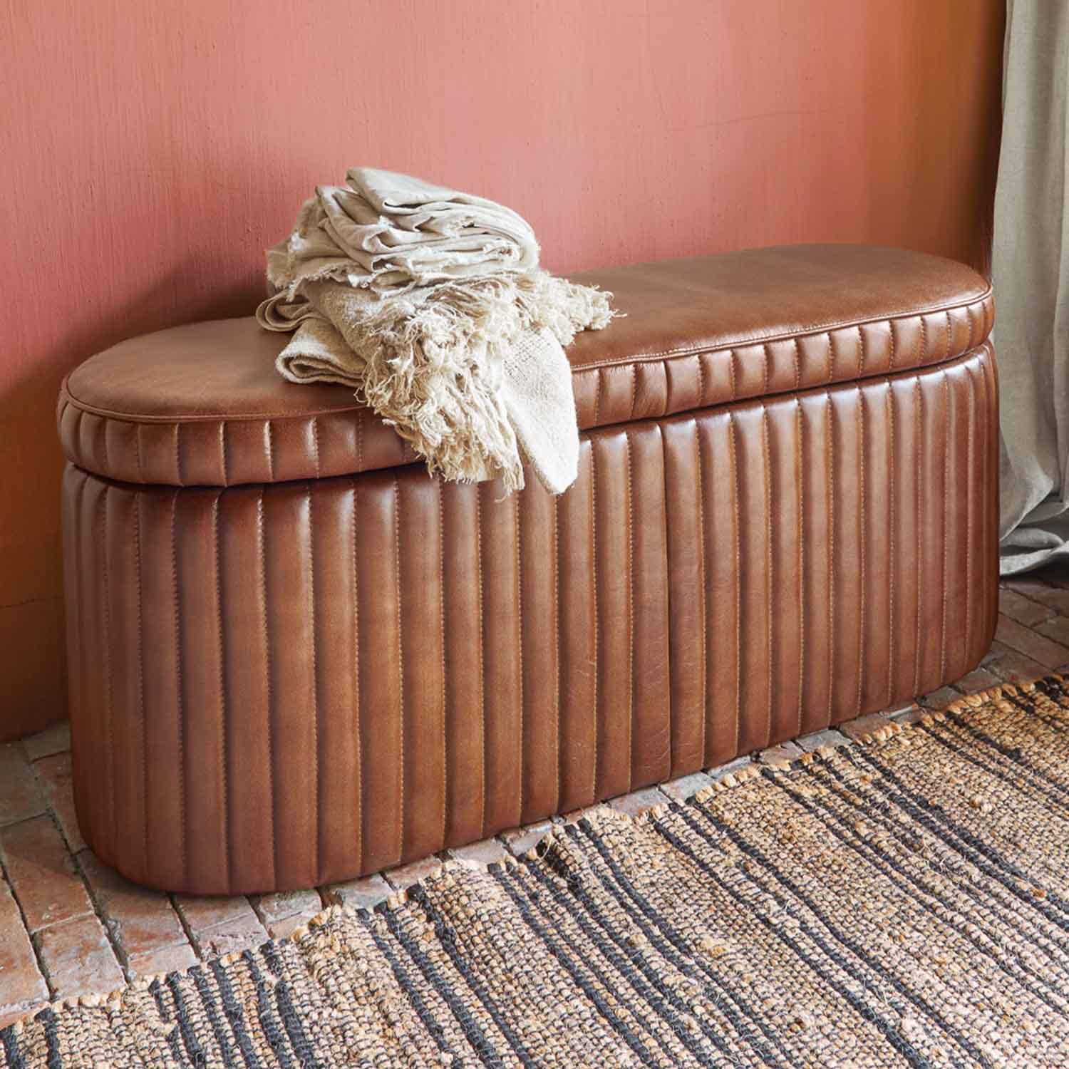 Pouf in pelle marrone trapuntata con coperte crema su sfondo di parete rosa e tappeto