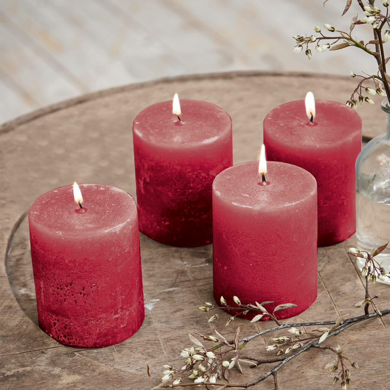 Set di 4 candele Virrans Quattro candele rosse in cera su tavolo di legno con decorazione floreale, atmosfera accogliente