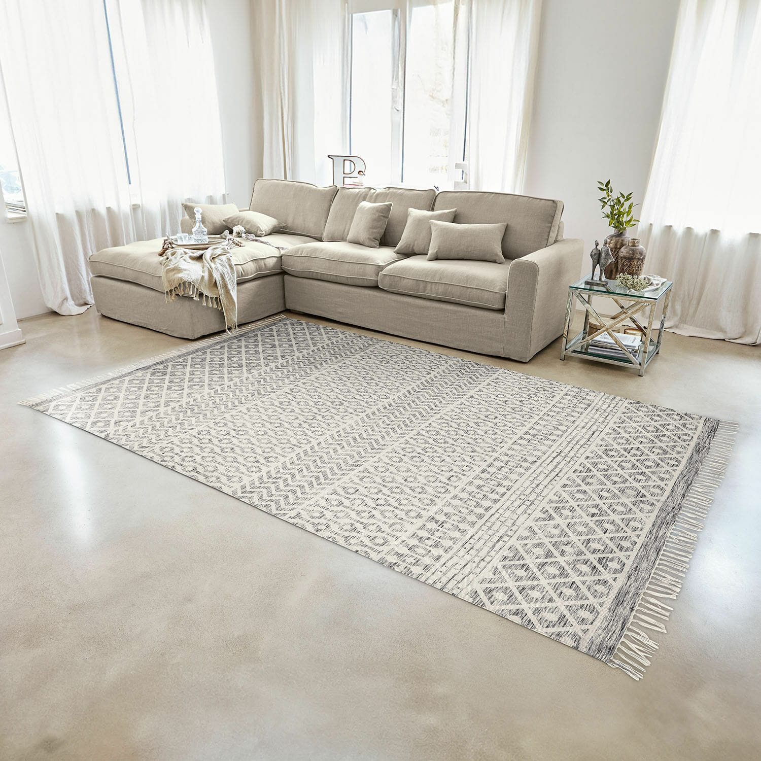 Tappeto per interni ed esterni Champigny Divano angolare beige in tessuto in soggiorno luminoso con tappeto a motivi geometrici e tavolino in vetro