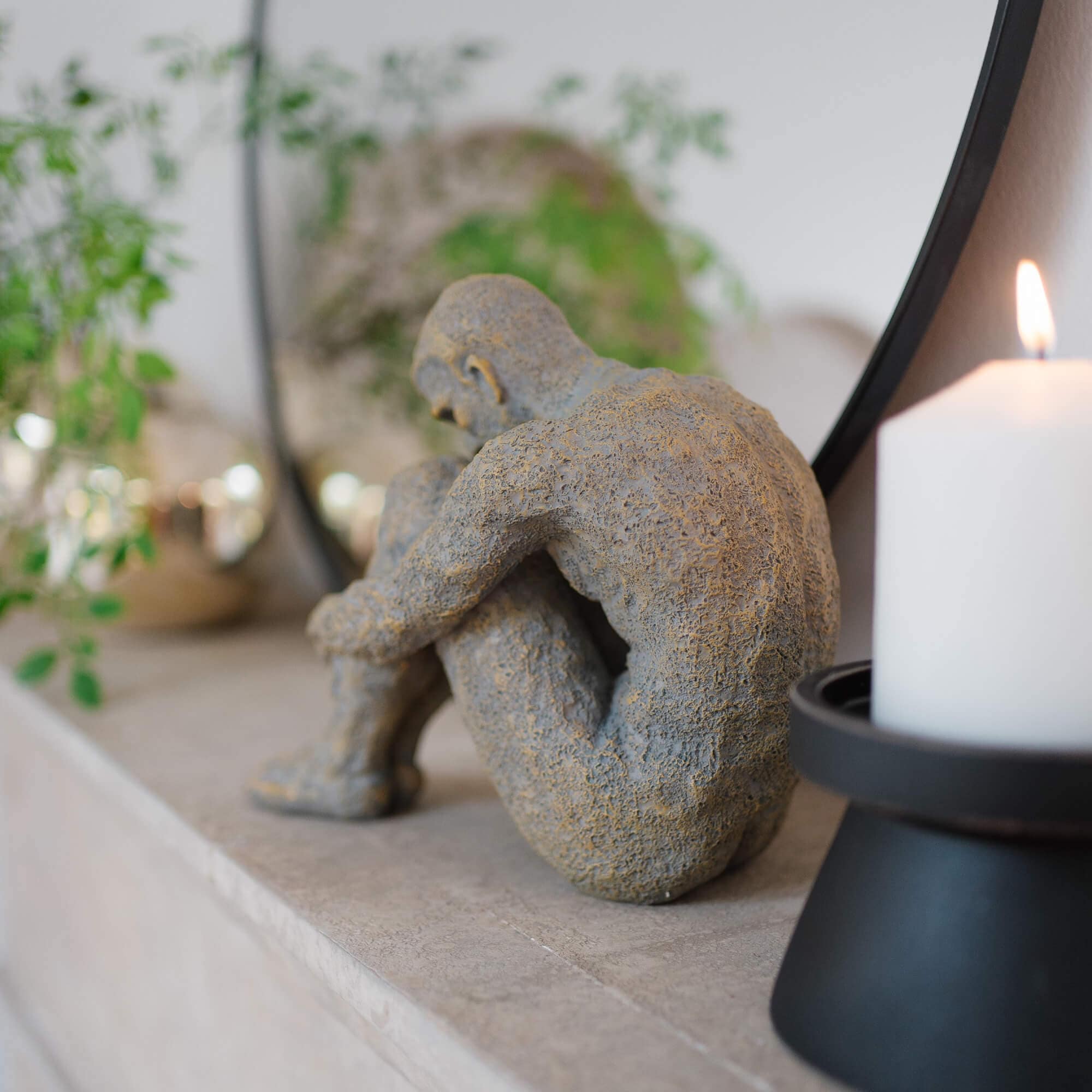 Scultura in pietra grigia di figura seduta su mensola in marmo con candela bianca