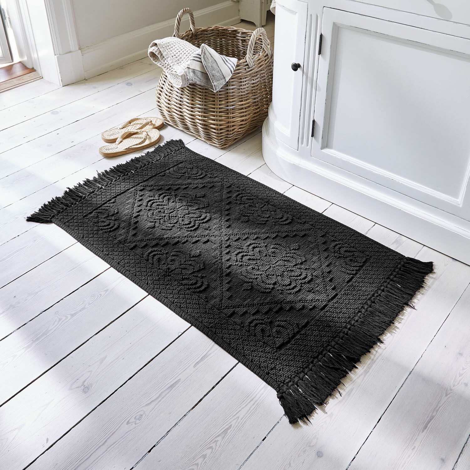Tappeto in cotone nero con frange e motivo geometrico su pavimento in legno chiaro