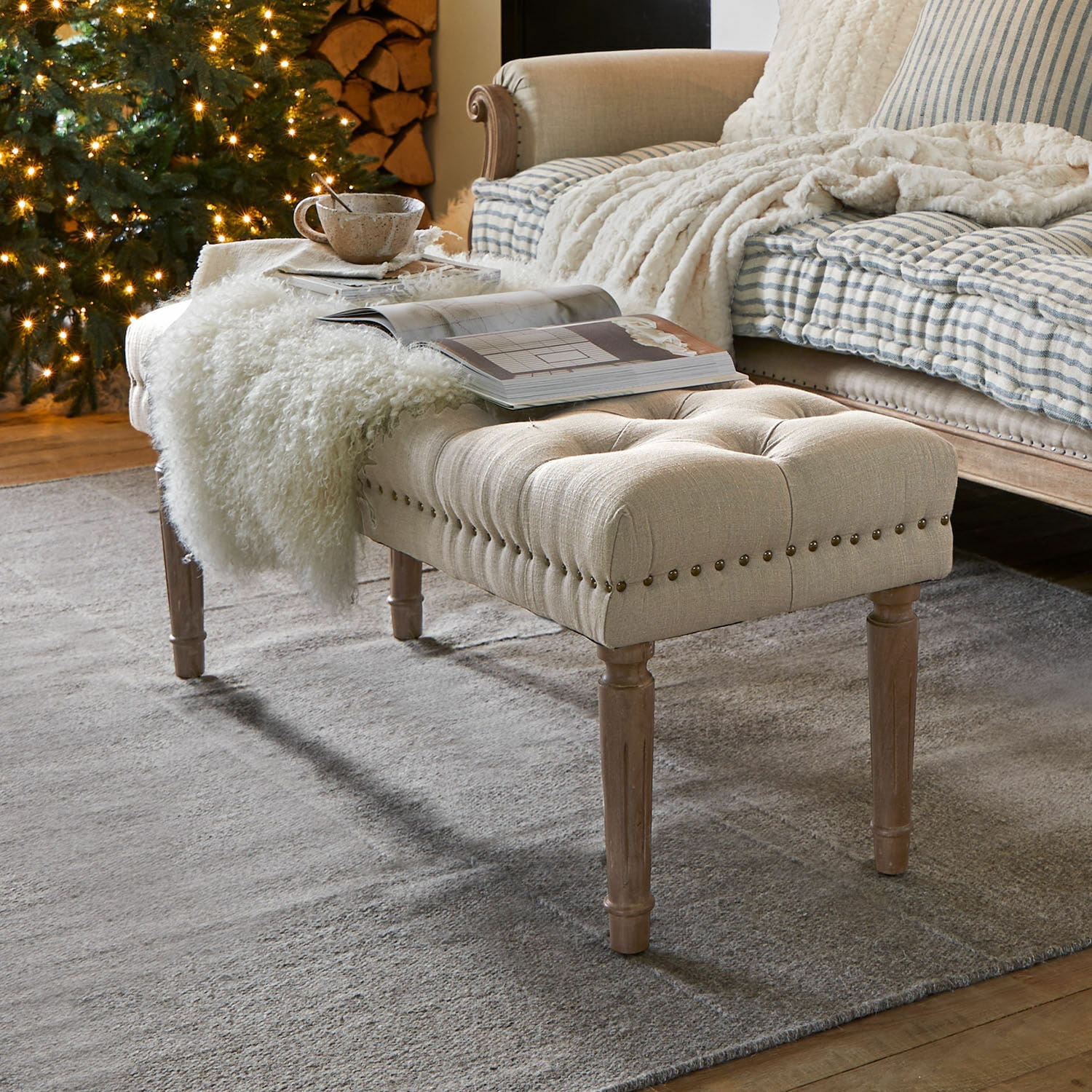 Panca Brookfield Panca imbottita beige con gambe in legno su tappeto grigio in soggiorno accogliente con albero di Natale