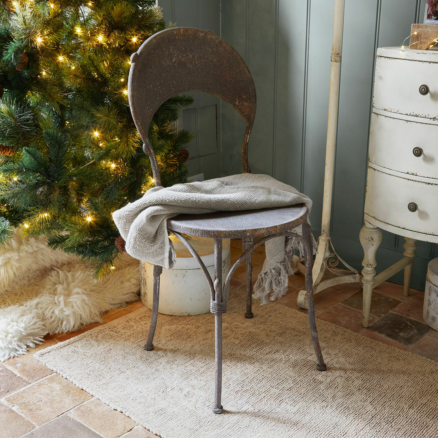 Sedia Delivora Sedia rustica in metallo arrugginito con coperta grigia vicino ad albero di Natale illuminato e tappeto