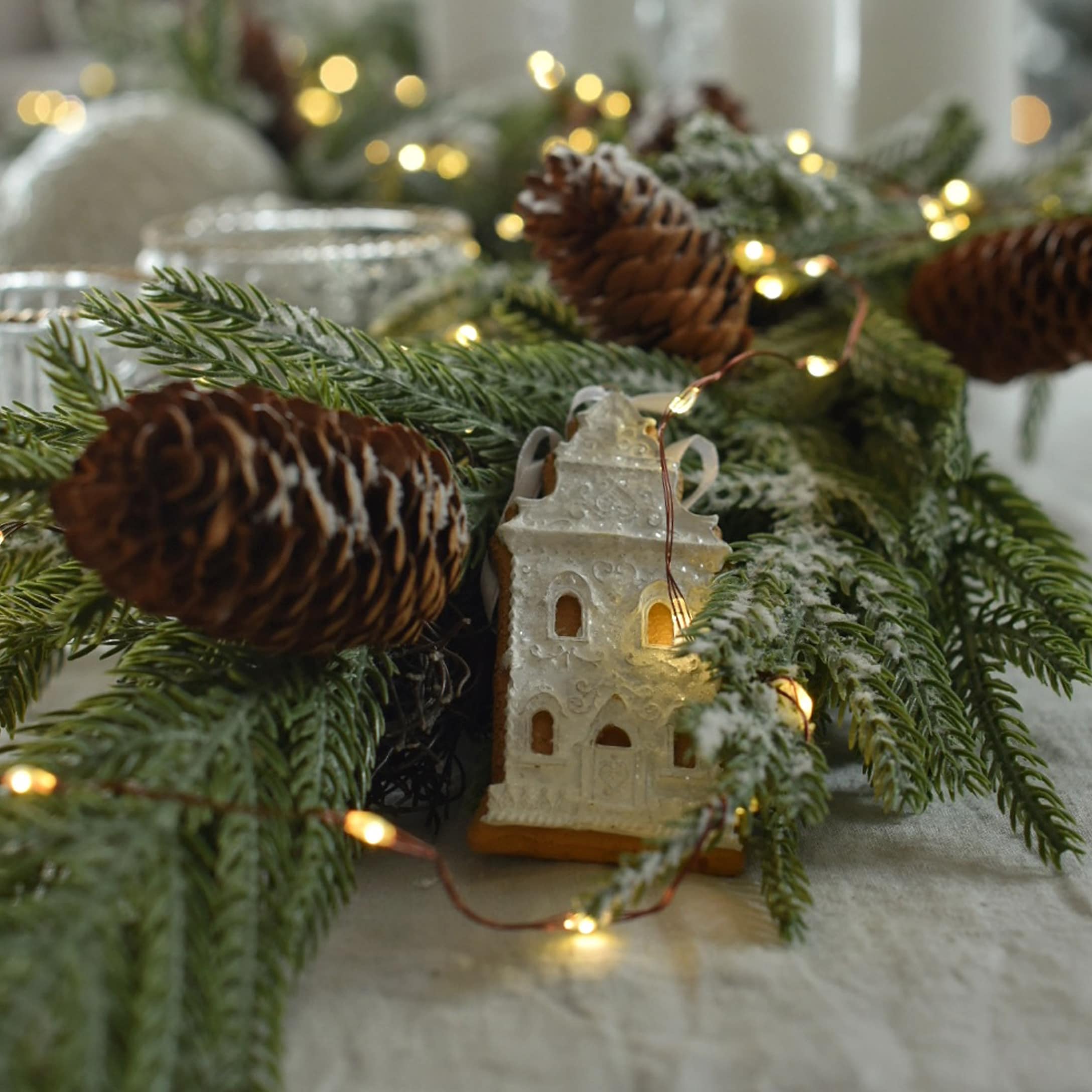 Decorazione natalizia con rami verdi, pigne e casetta di pan di zenzero illuminata su tavolo