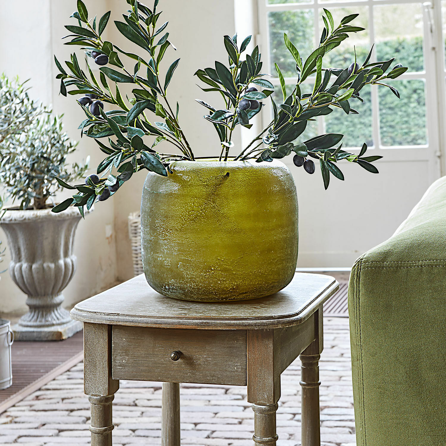 Vaso Hilvento Vaso in ceramica verde su tavolo in legno con rami decorativi di ulivo in interno luminoso