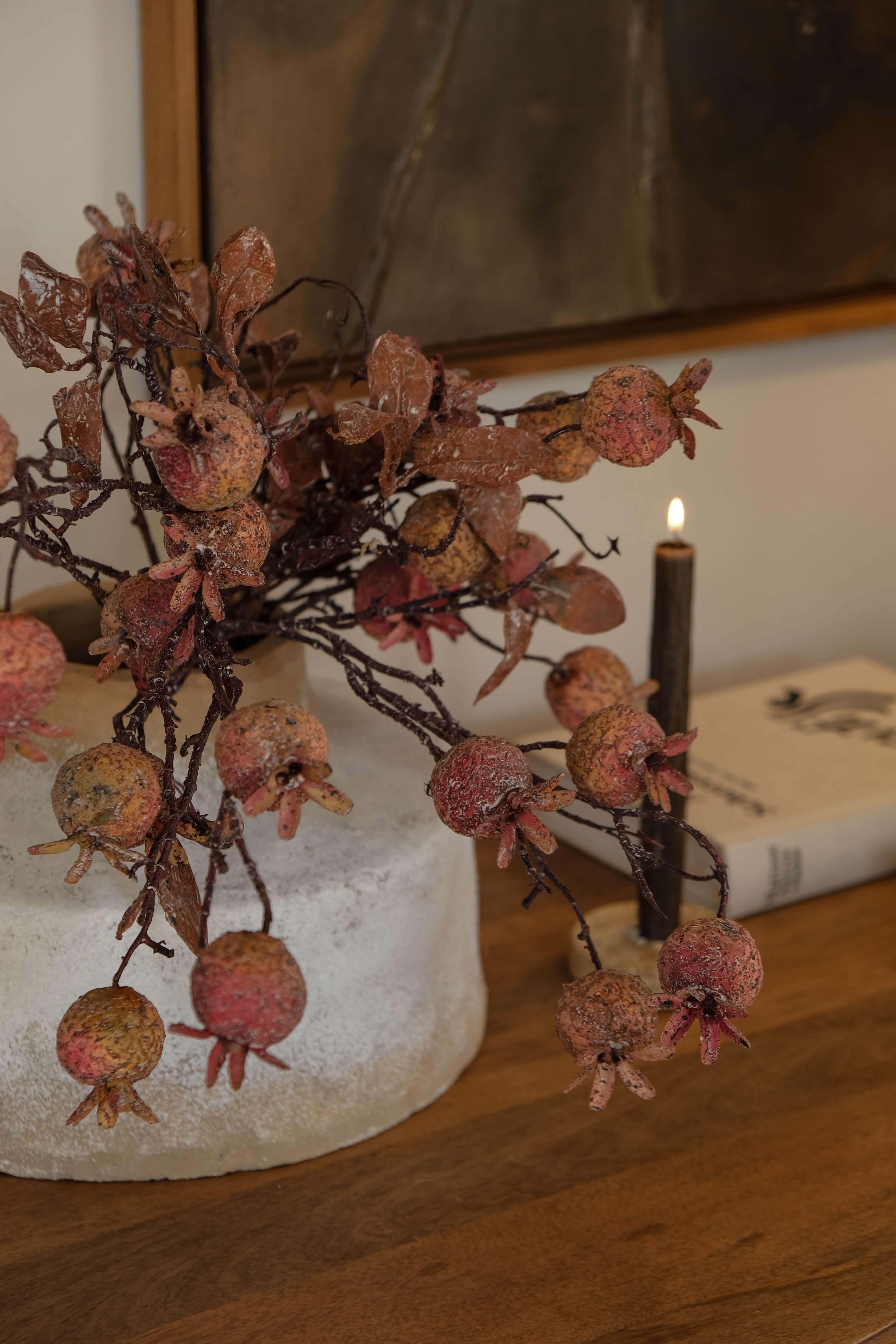 Ramo decorativo con frutti di melograno in tonalità naturali su base chiara su tavolo in legno