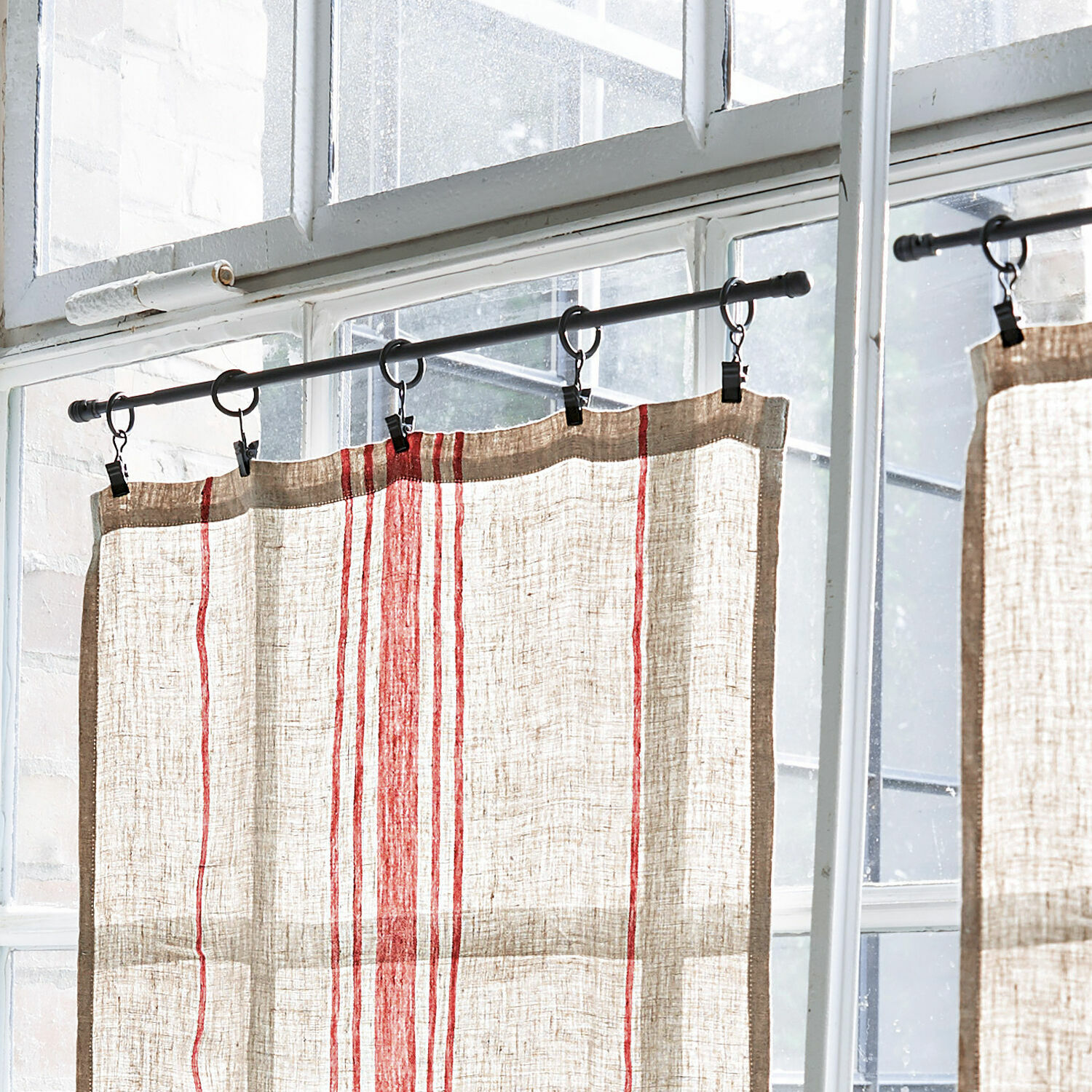 Tenda in lino color naturale con strisce rosse appesa a bastone metallico davanti a finestra
