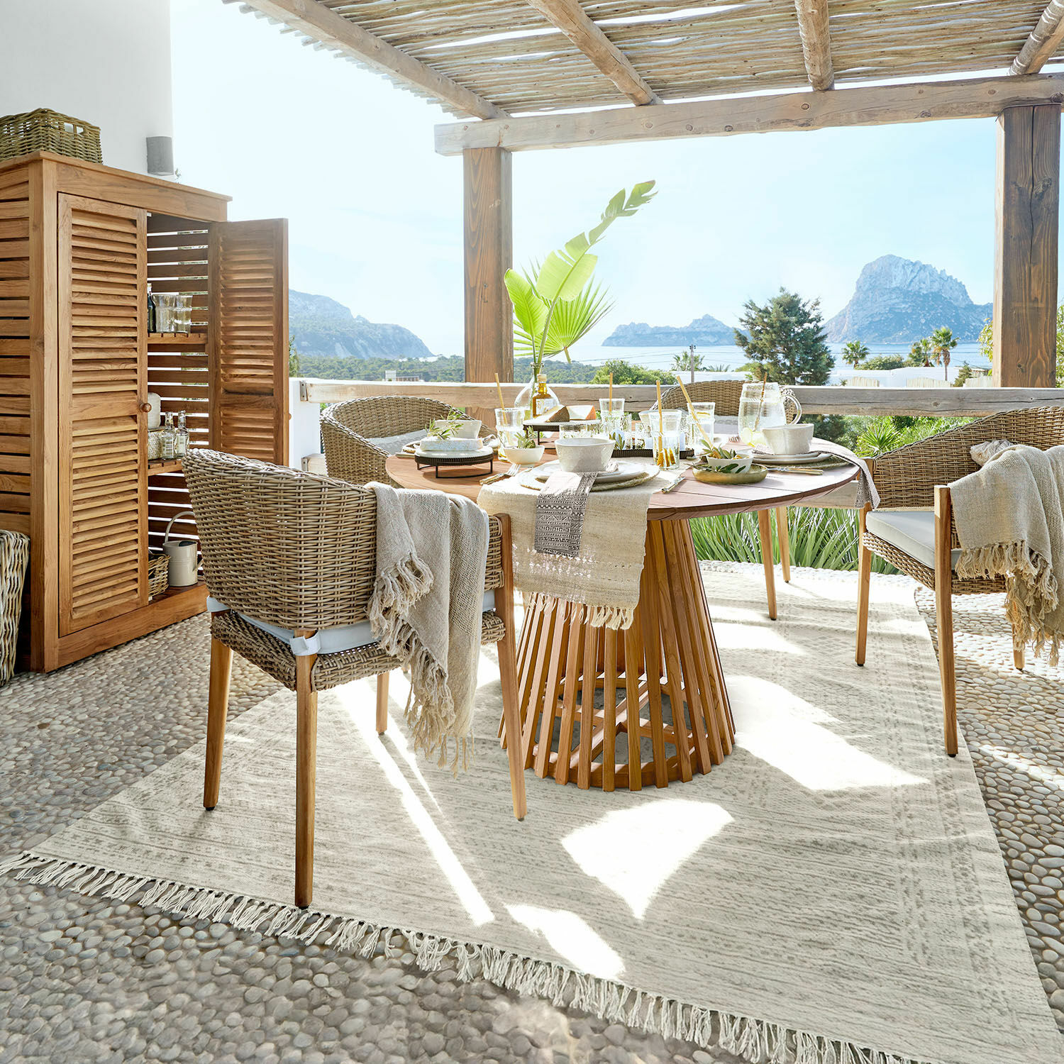 Tappeto per esterni Savagnac Zona pranzo in terrazza con tavolo in legno e sedie in vimini beige, vista mare e decorazione naturale