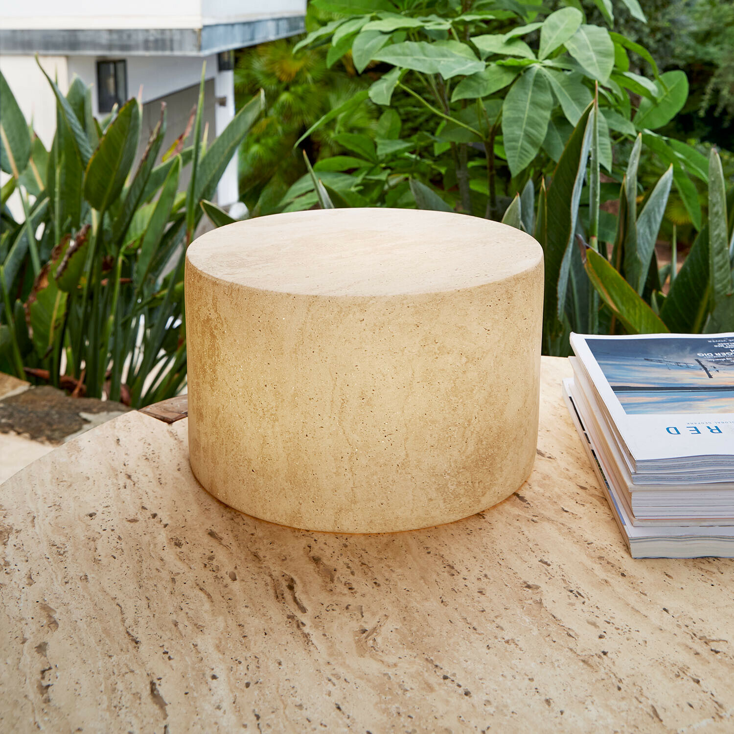 Tavolino rotondo in travertino beige su terrazza con piante verdi, pietra naturale