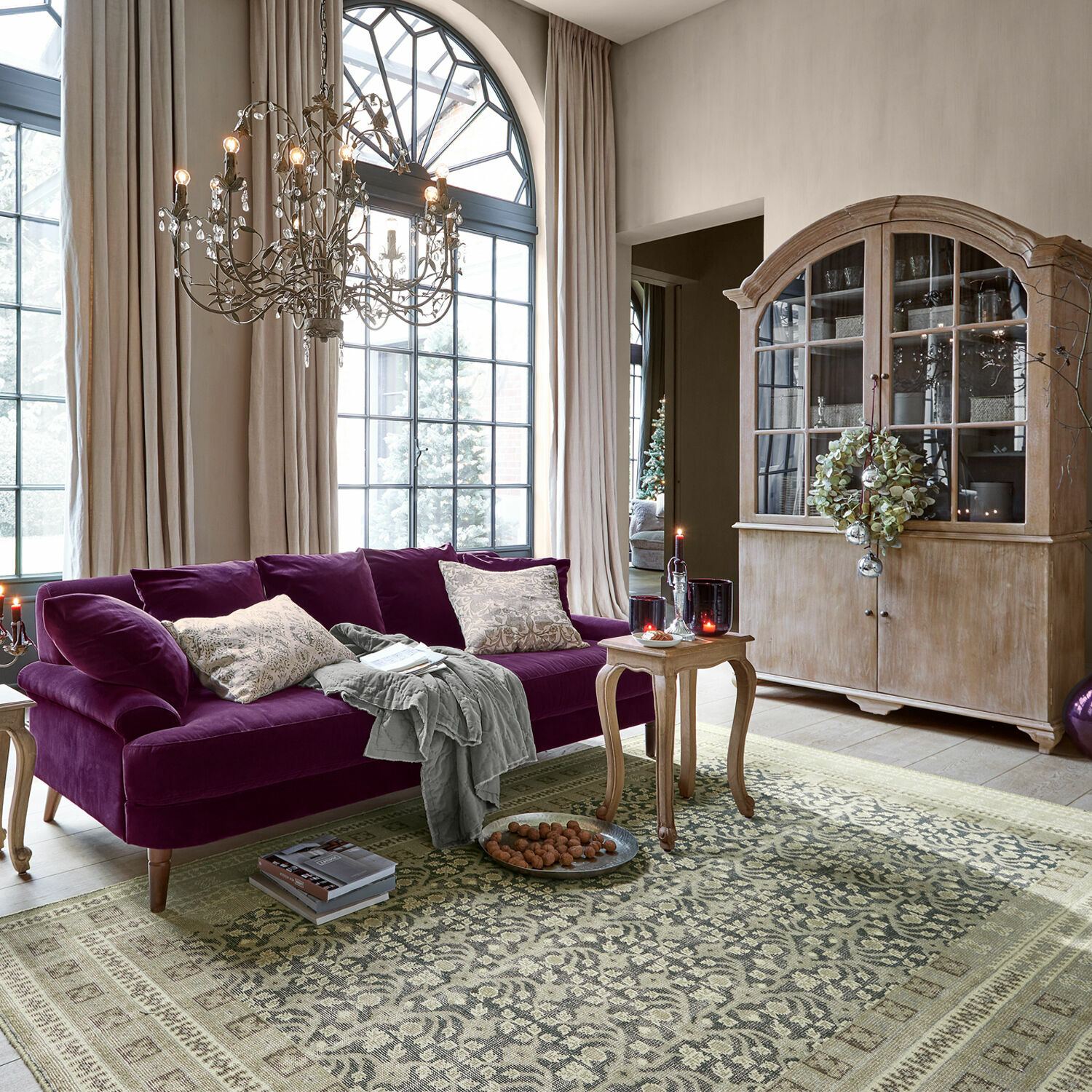 Tappeto Nadimah Soggiorno con divano viola in velluto e vetrina in legno davanti a grandi finestre e tappeto decorato