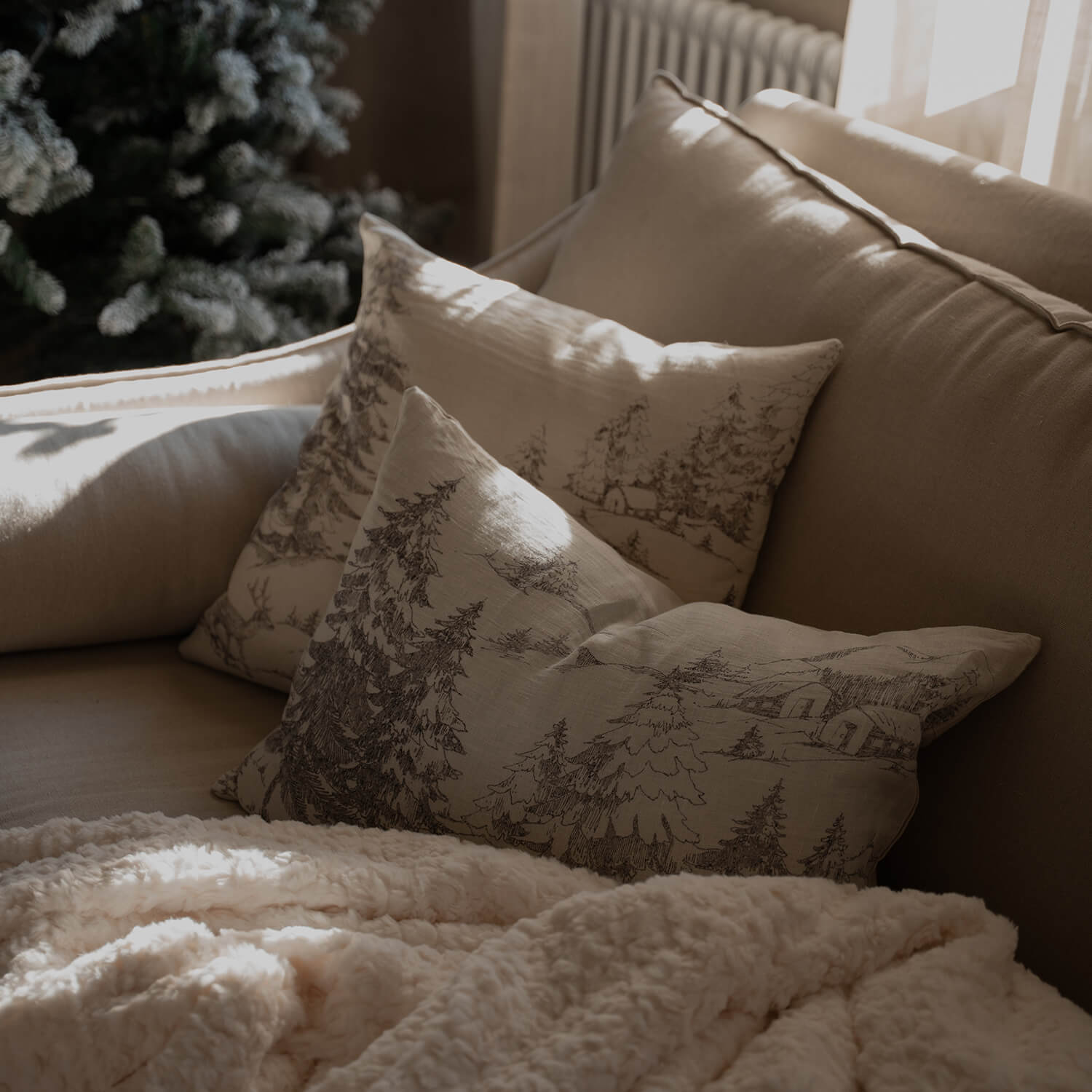 Divano beige con cuscini decorativi a motivo bosco e morbida coperta crema per soggiorno