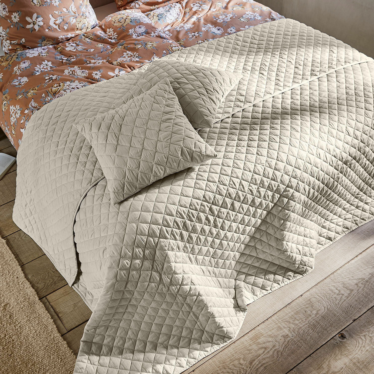 Trapunta Jolique Copriletto trapuntato beige con cuscini su letto in legno e biancheria da letto floreale