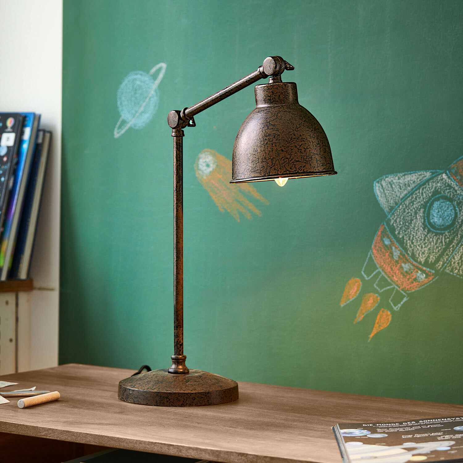 Lampada da tavolo Cheeklee Lampada da tavolo in metallo effetto ruggine su scrivania in legno davanti a lavagna verde con disegni spaziali