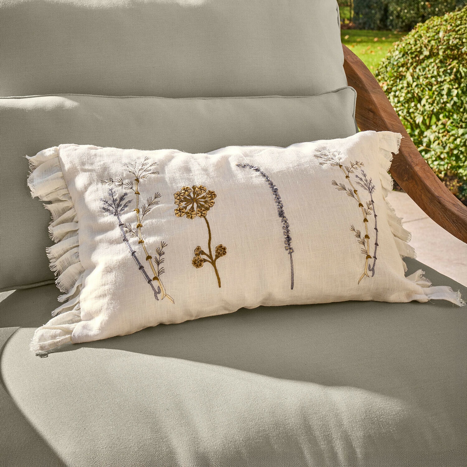 Copricuscino Quélivane Cuscino beige in lino con ricami floreali e frange su poltrona da giardino verde