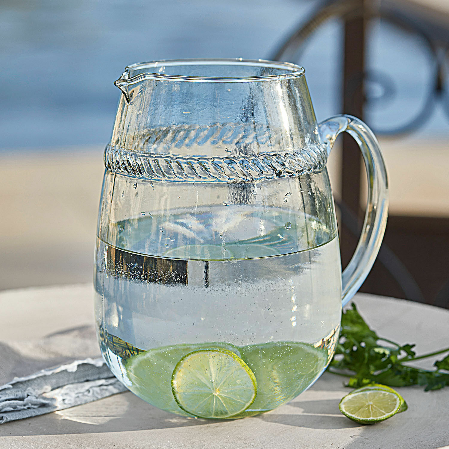 Caraffa Beiras Brocca in vetro trasparente con acqua e fette di lime su tavolo da giardino