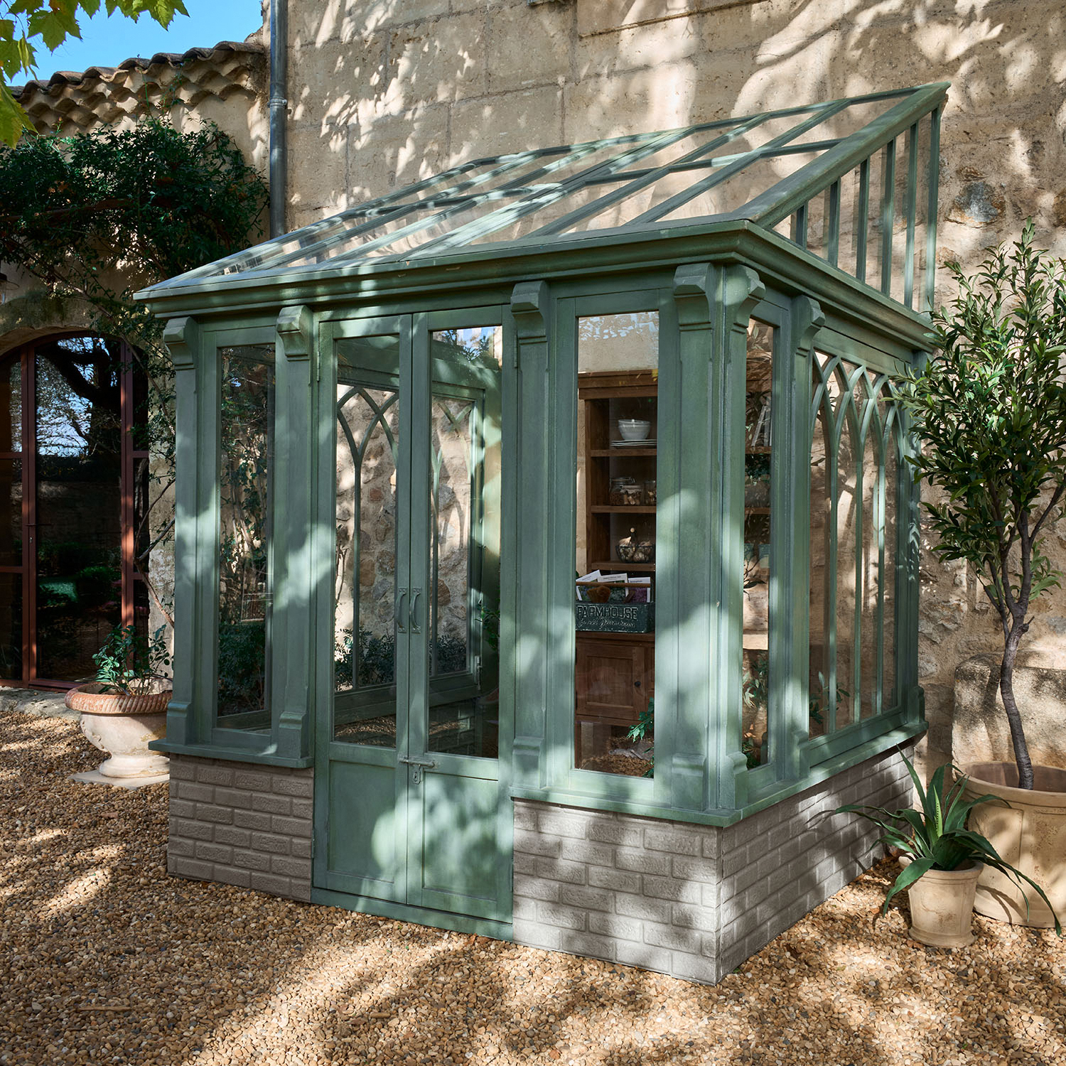 Serra in legno verde con tetto in vetro trasparente e base in mattoni nel giardino