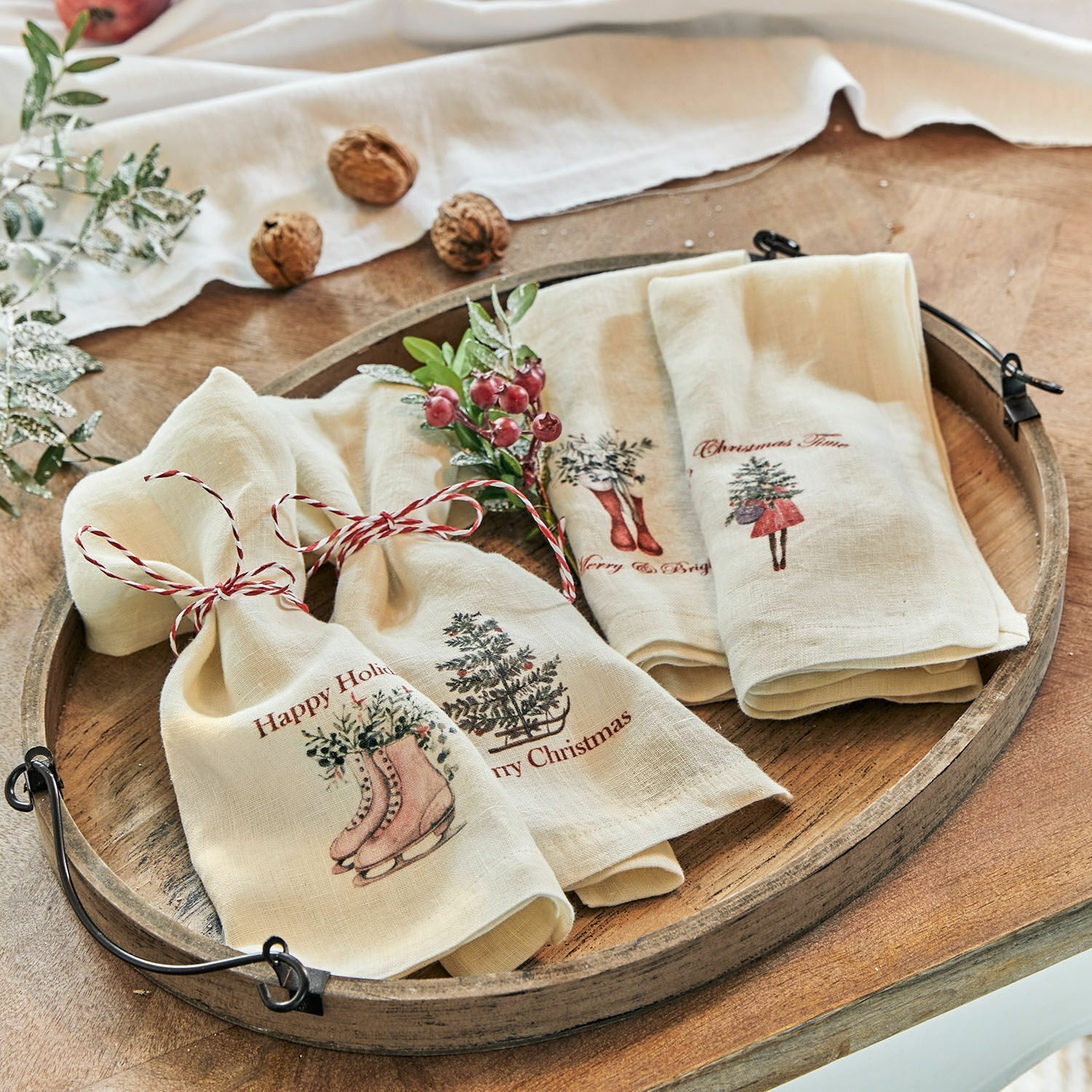 Set di 4 tovaglioli Merry & Bright Strofinacci in lino crema con motivi natalizi e cordoncino rosso su vassoio di legno rustico