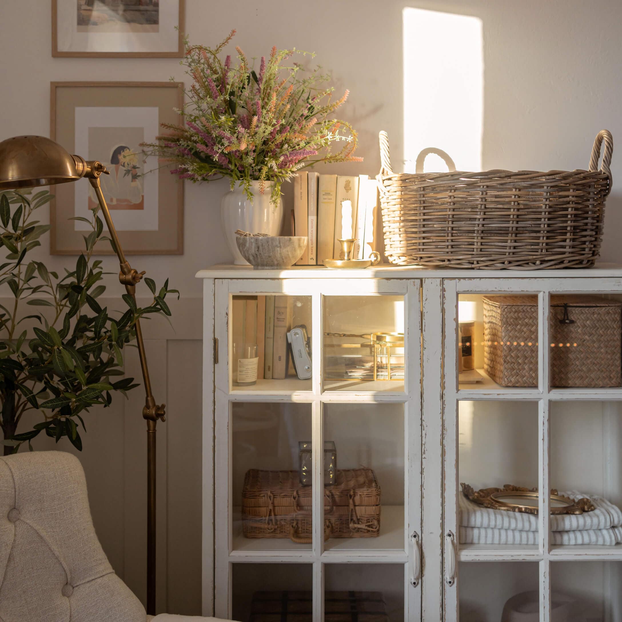 Credenza bianca in legno con ante in vetro, cesta in vimini e decorazioni in soggiorno luminoso