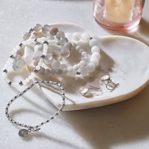 Set di gioielli con perle bianche e grigie su un vassoio di marmo a forma di cuore